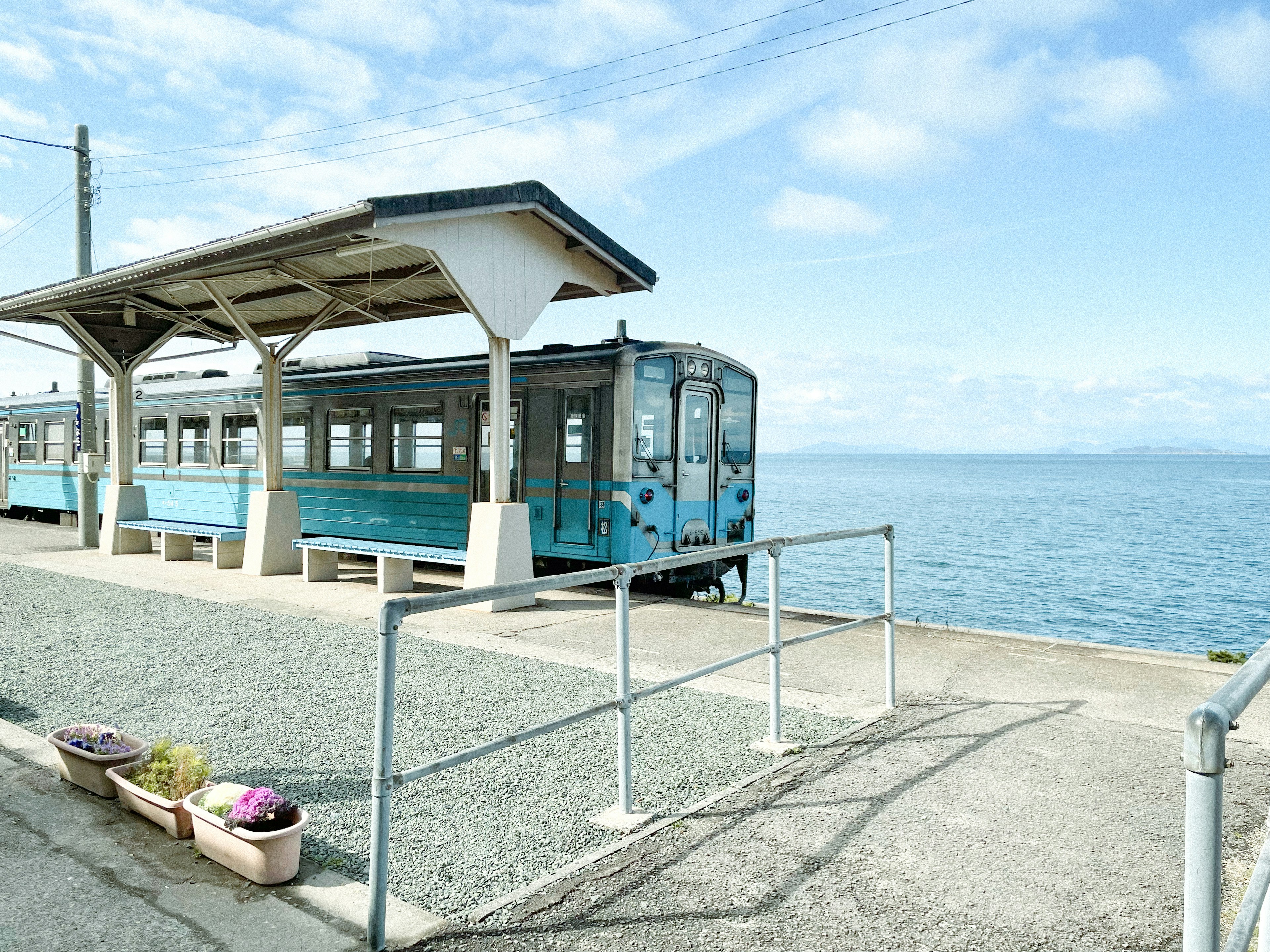 一列藍色火車停靠在海邊的車站，天空晴朗