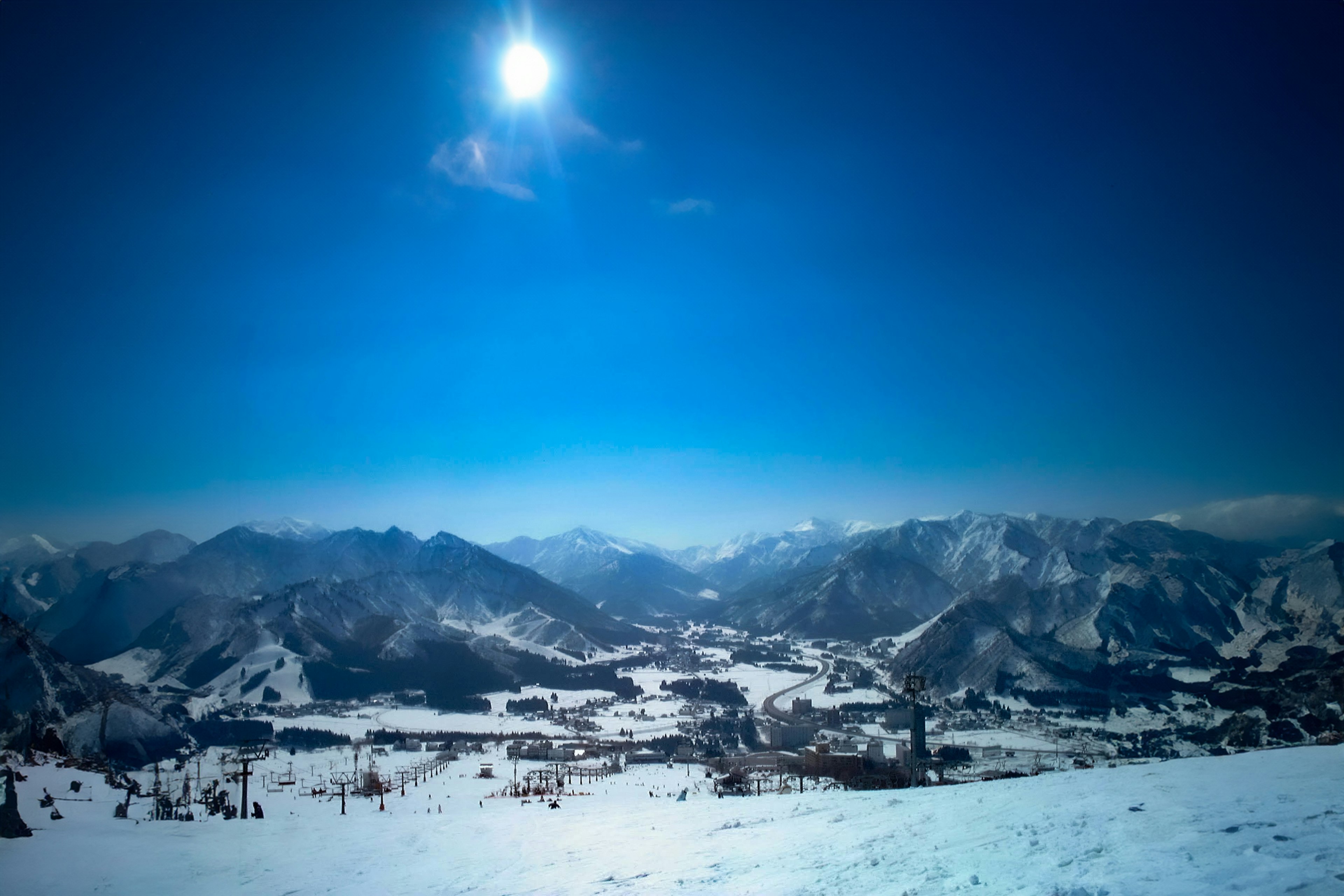 青空の下、雪に覆われた山々のパノラマビュー、明るい太陽が輝く