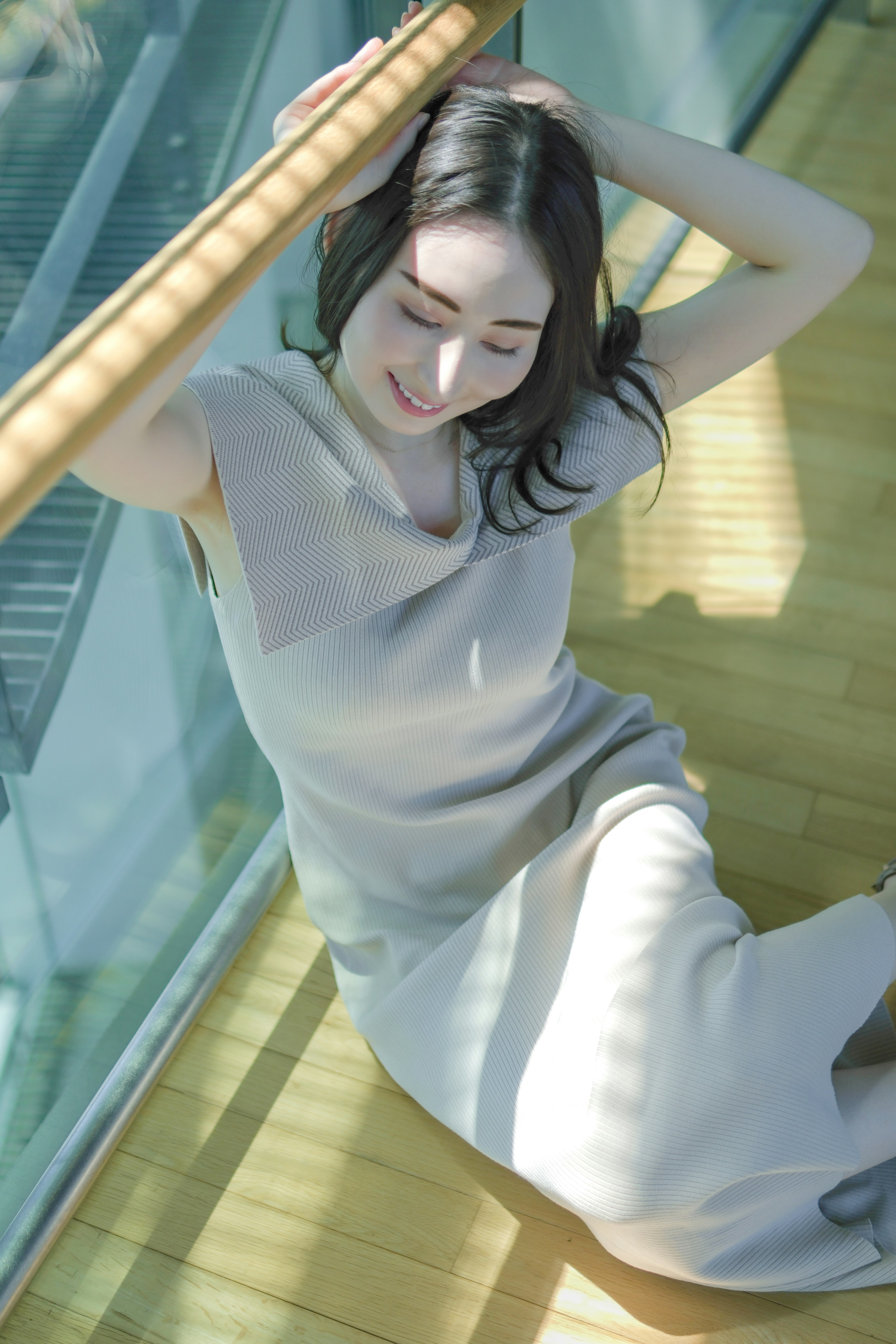 Una mujer sonriendo con un vestido beige suave frente a un fondo de vidrio transparente