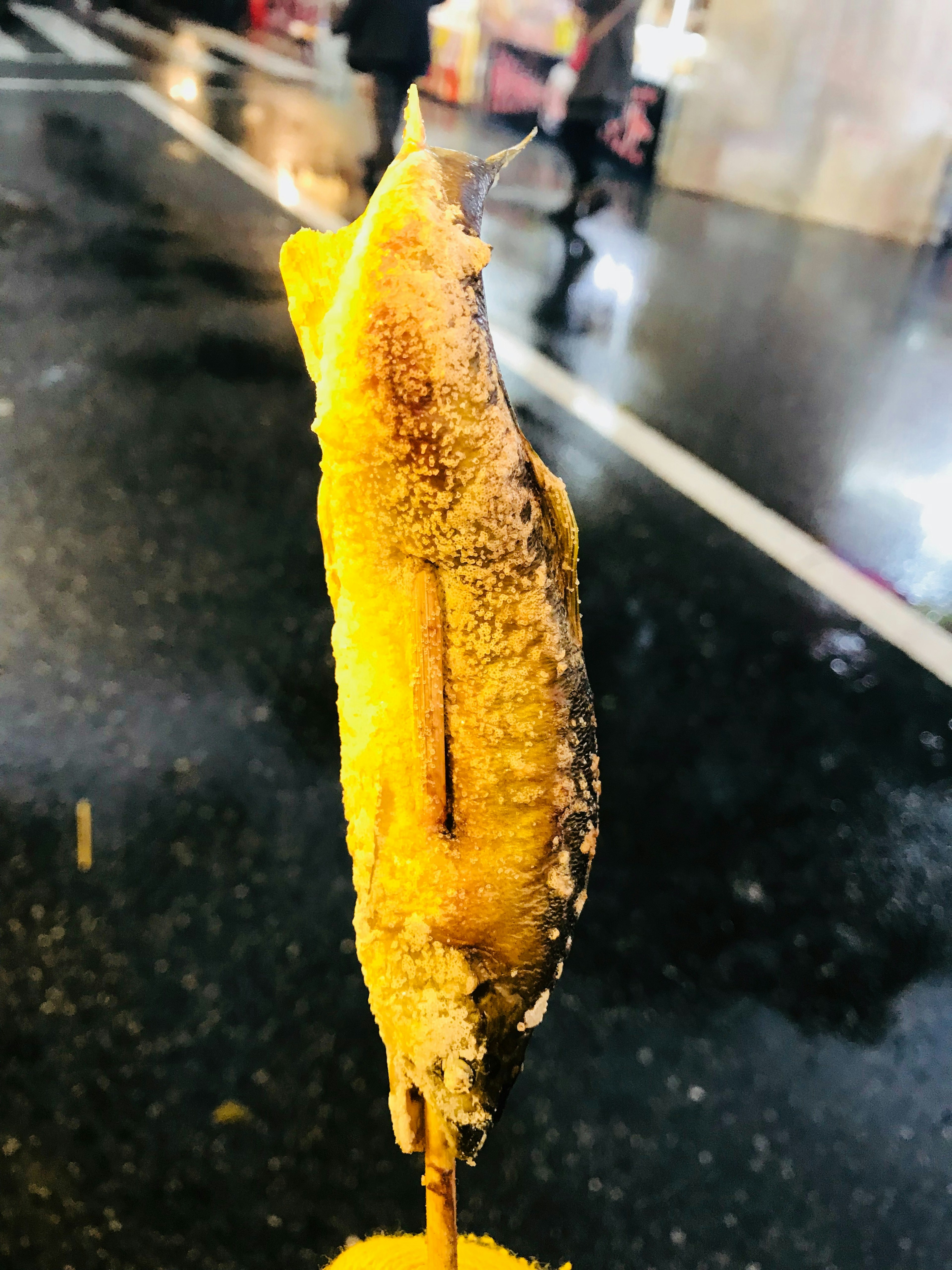 Fried banana snack on a stick standing on a wet road