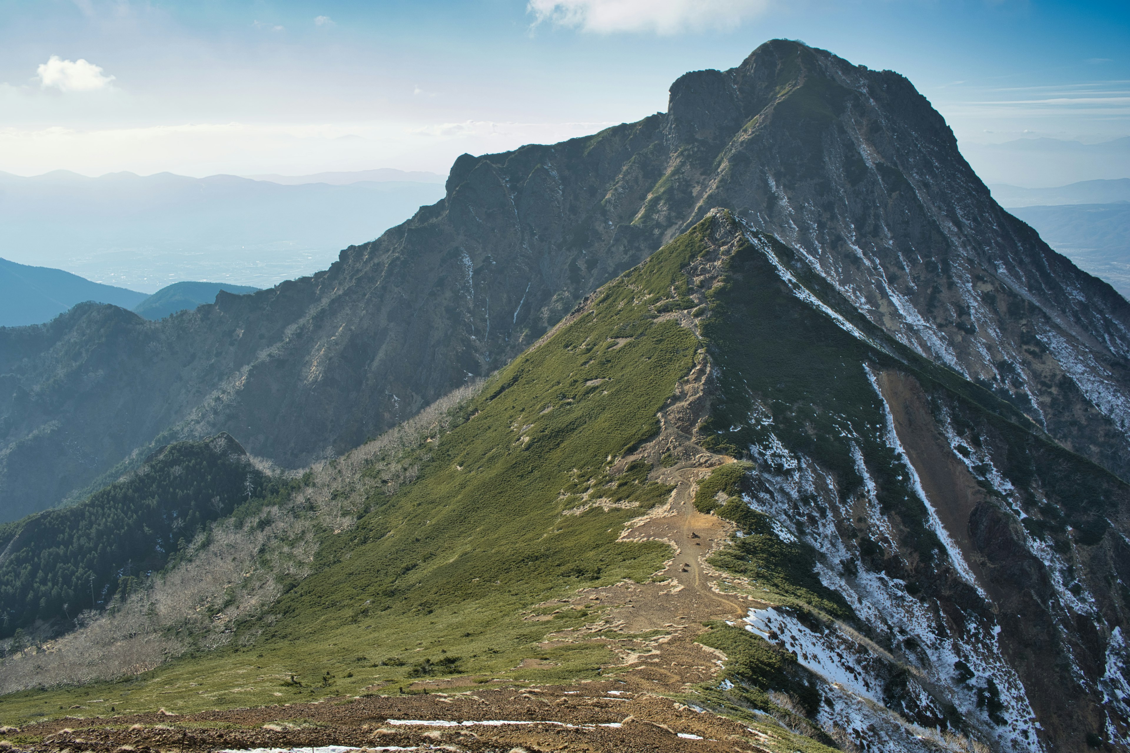 Vista escénica de montaña con laderas verdes y parches de nieve bajo un cielo azul