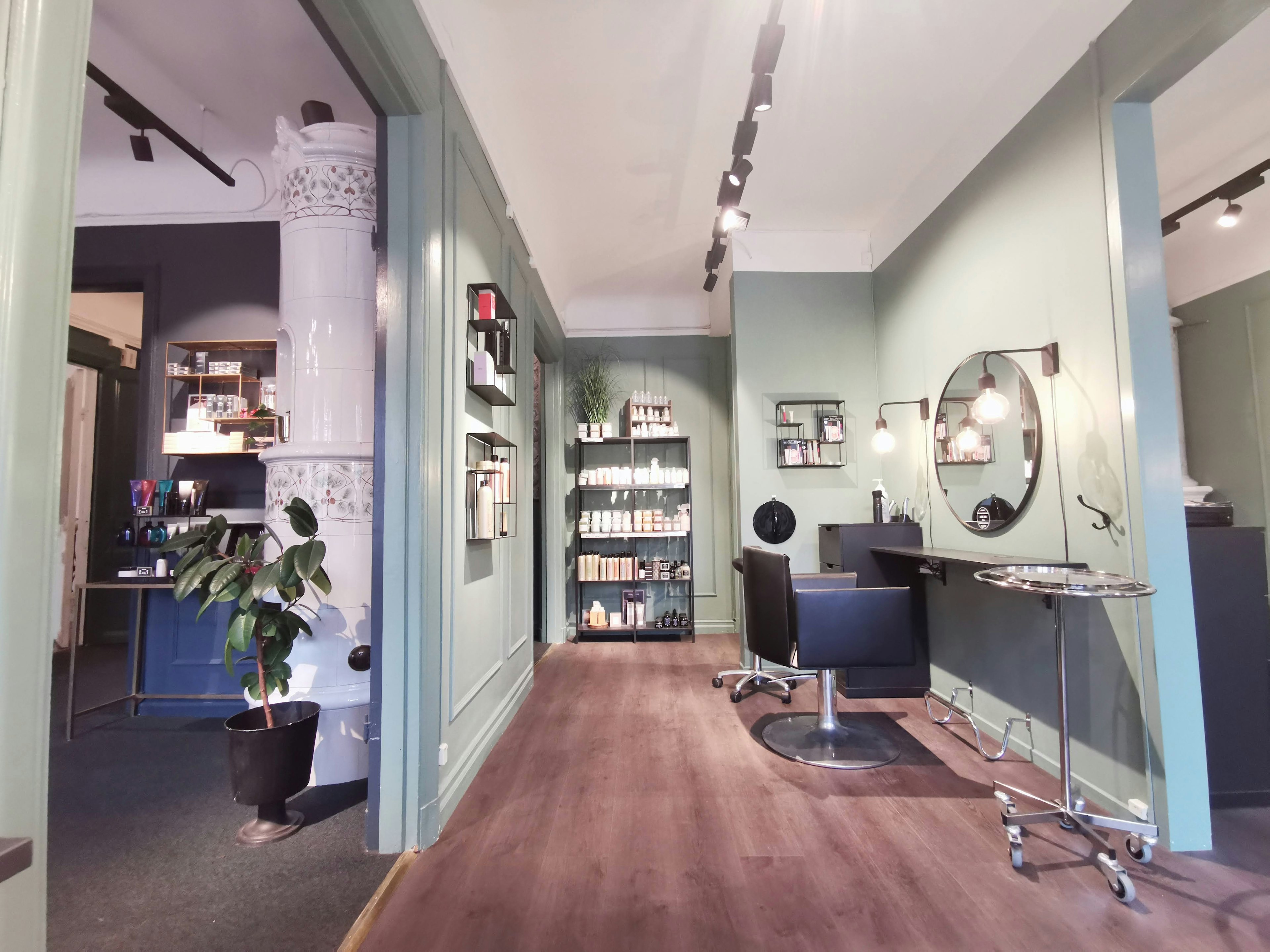 Intérieur d'un salon avec des murs verts présentant un espace de coiffure avec un miroir et une chaise