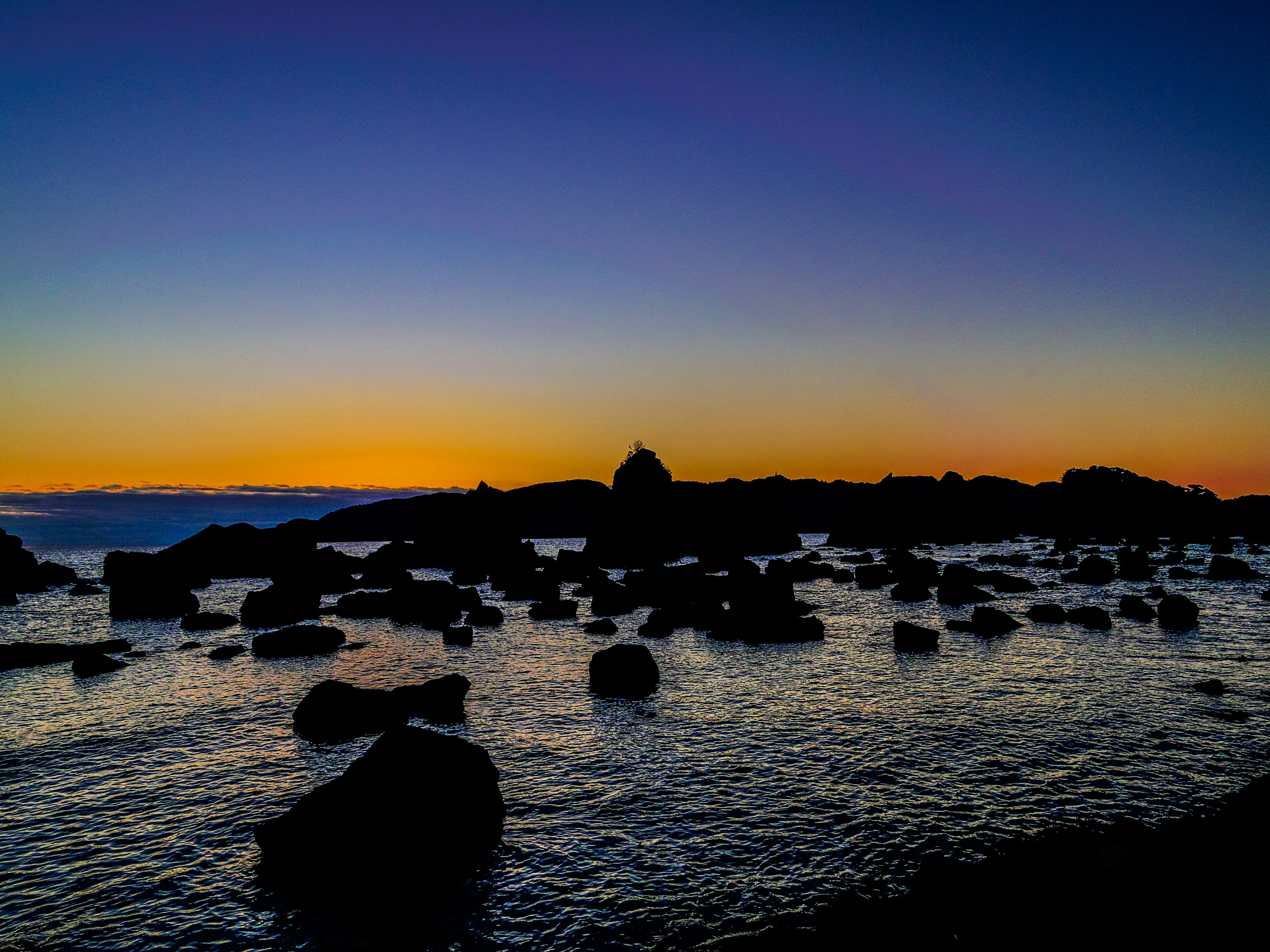 美麗的日落海岸線，岩石和寧靜的水面