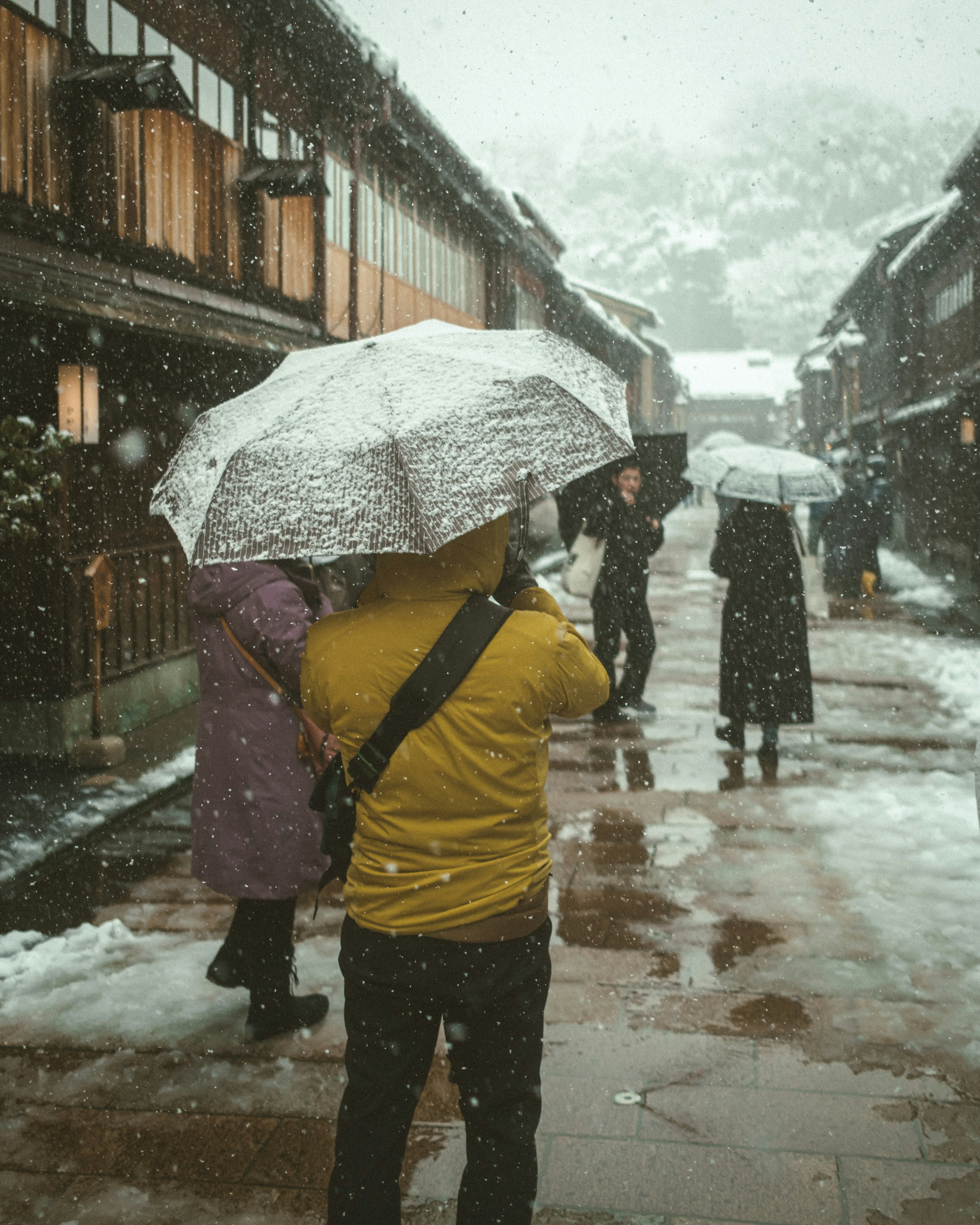 People walking with umbrellas in the snow on a historic street