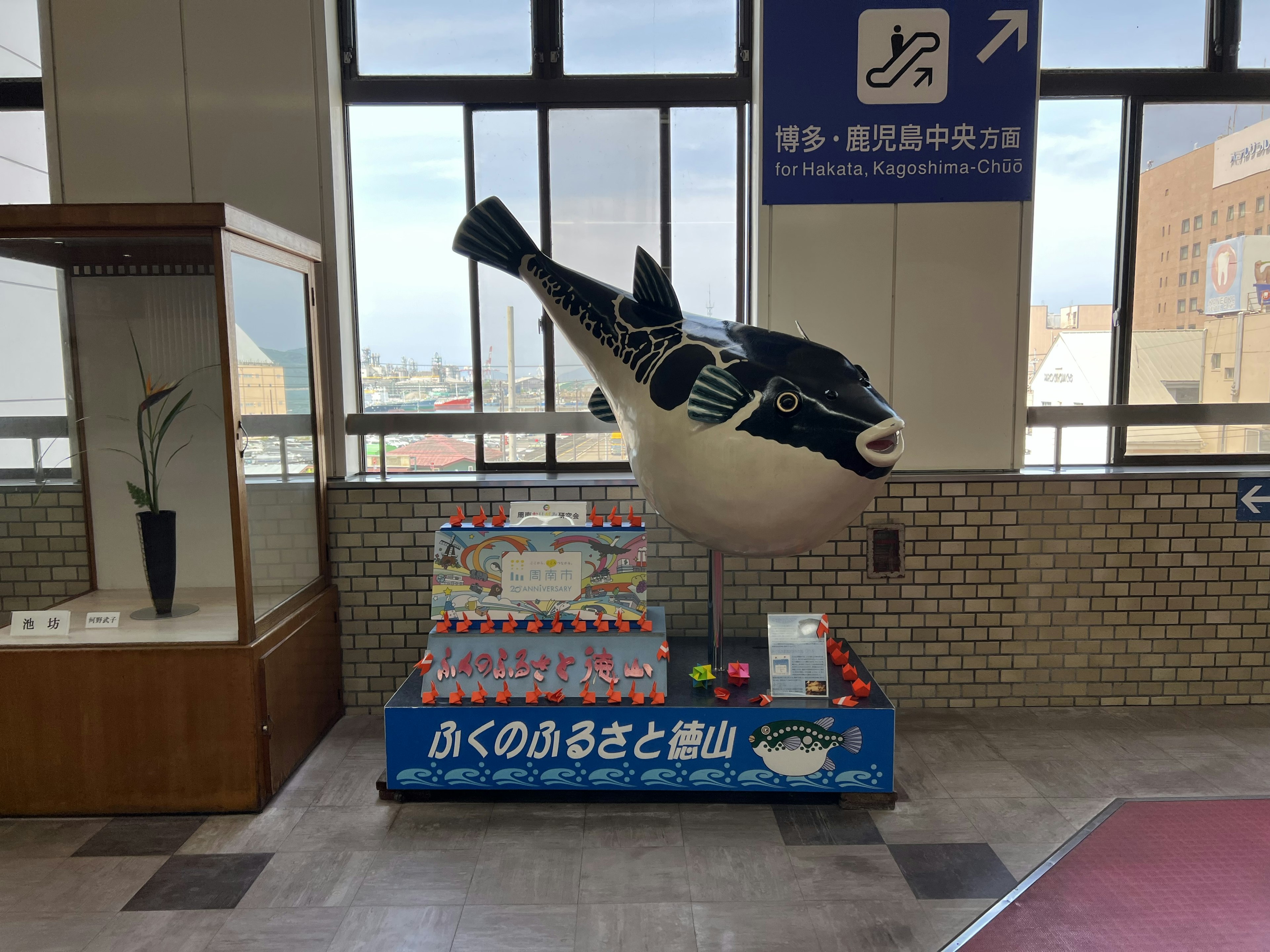 Large pufferfish sculpture in a station lobby with a display of tourist brochures