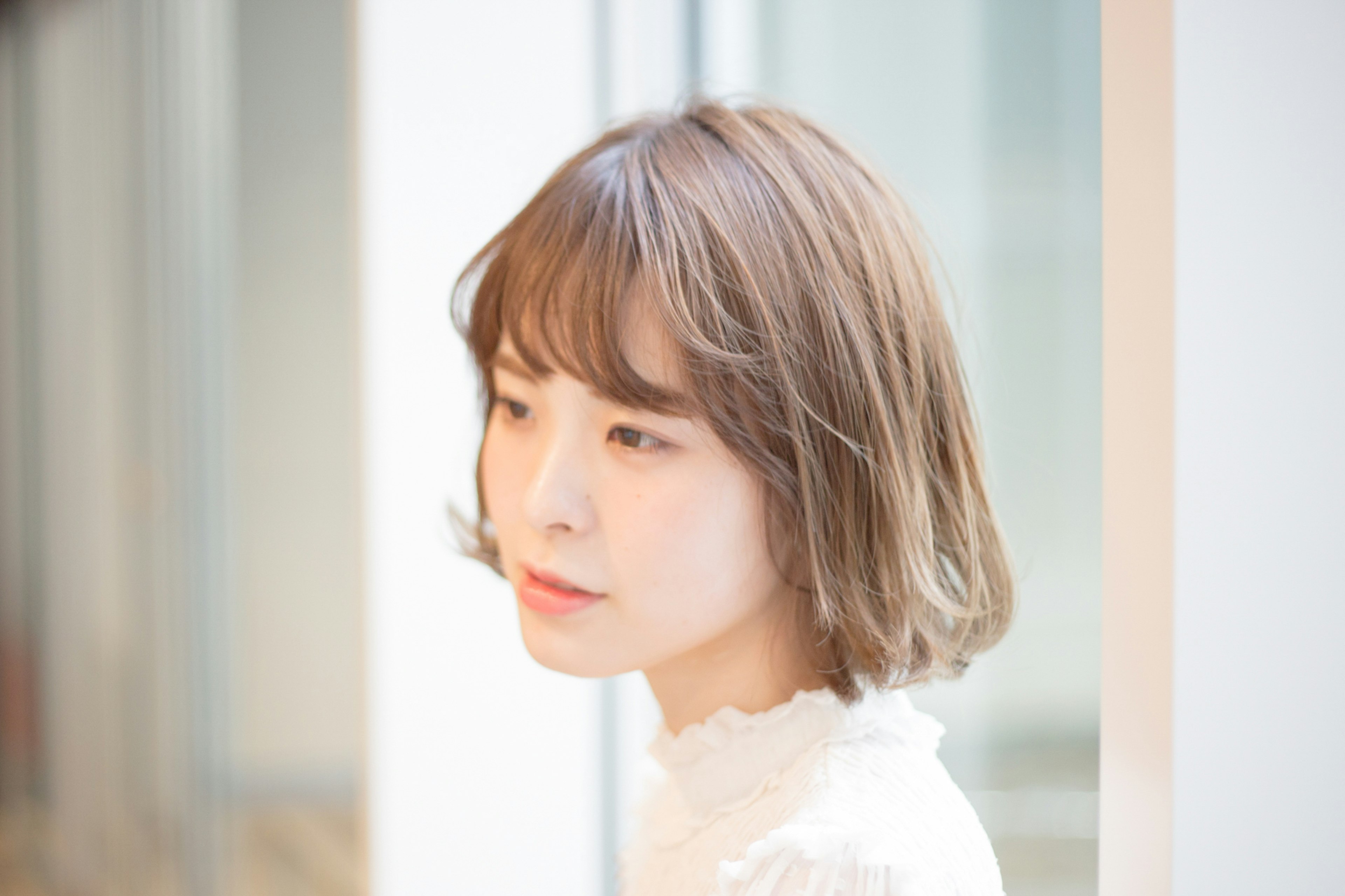 Young woman in profile, soft hairstyle, white top, bright background