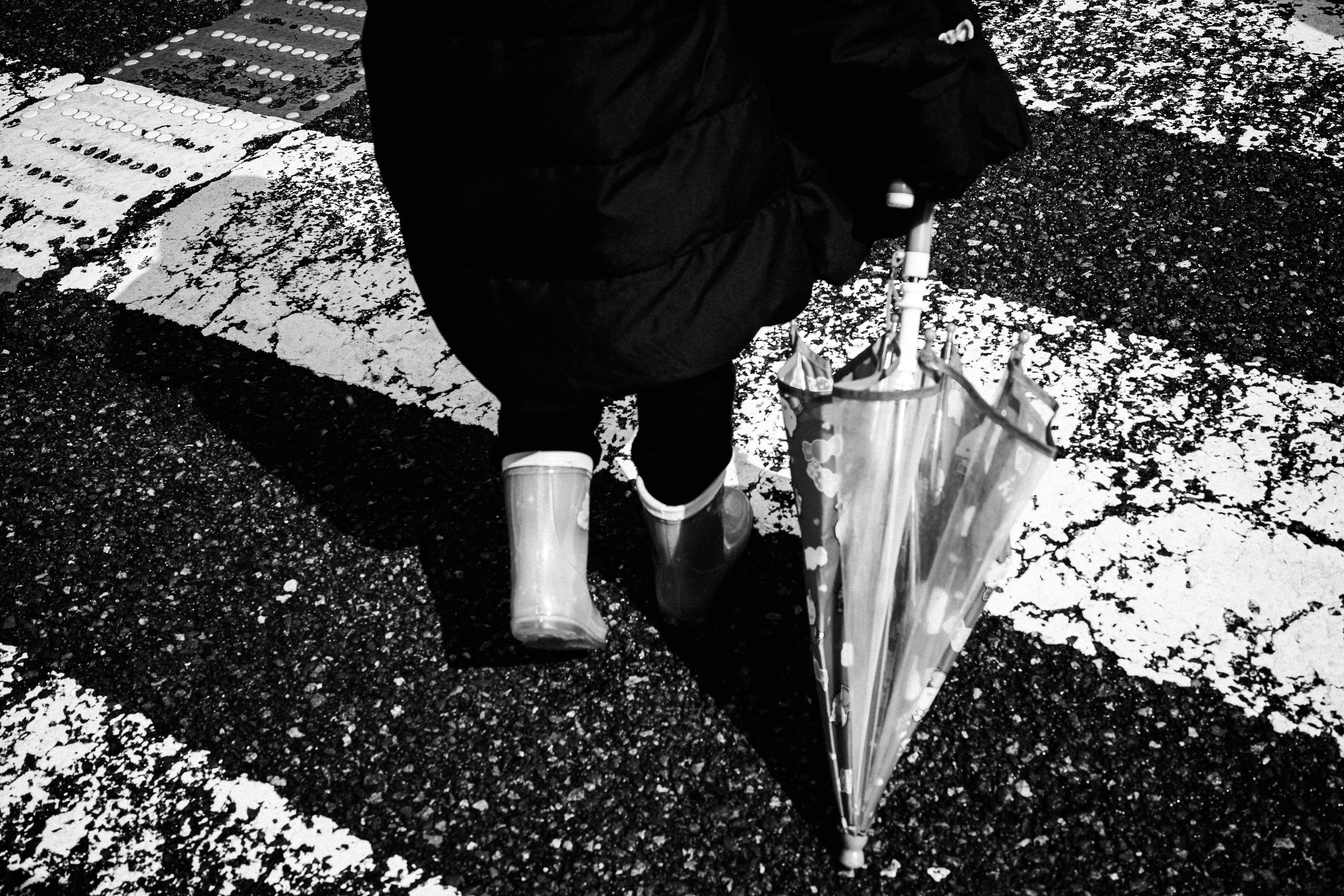 Personne marchant sur un passage piéton en noir et blanc avec un parapluie