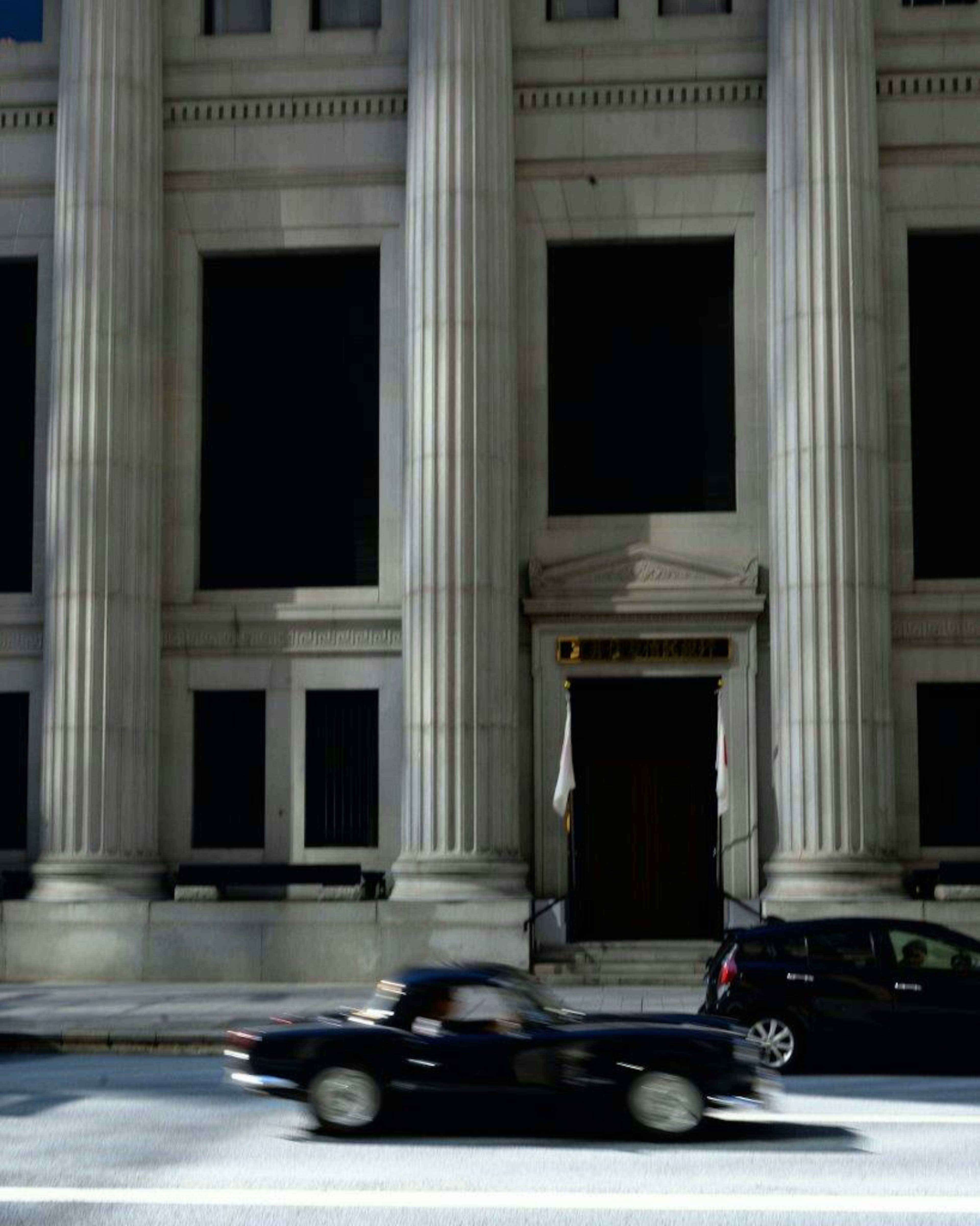 Edificio con columnas clásicas y un coche negro que pasa