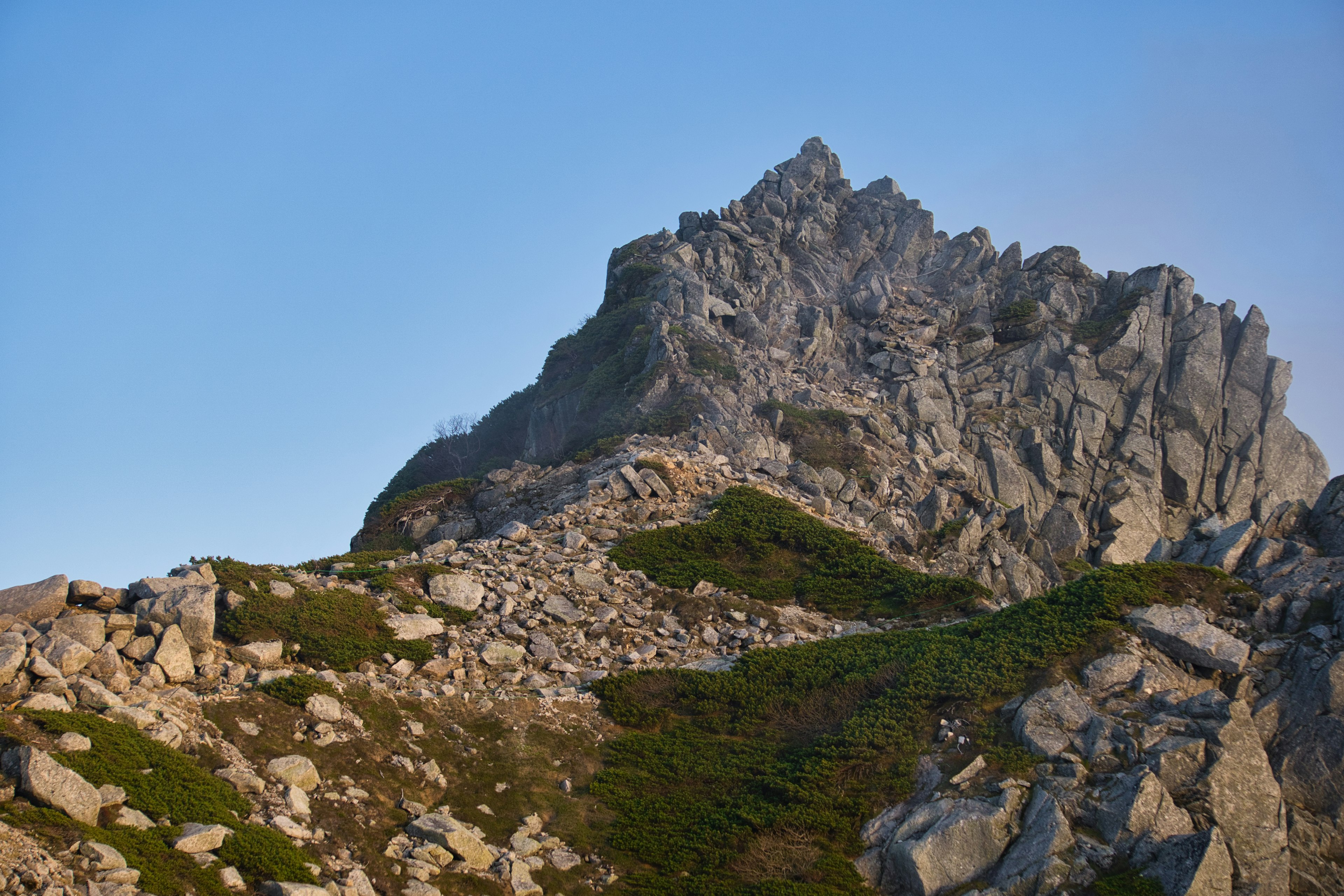 Paesaggio montano con terreno roccioso e vegetazione sotto un cielo azzurro