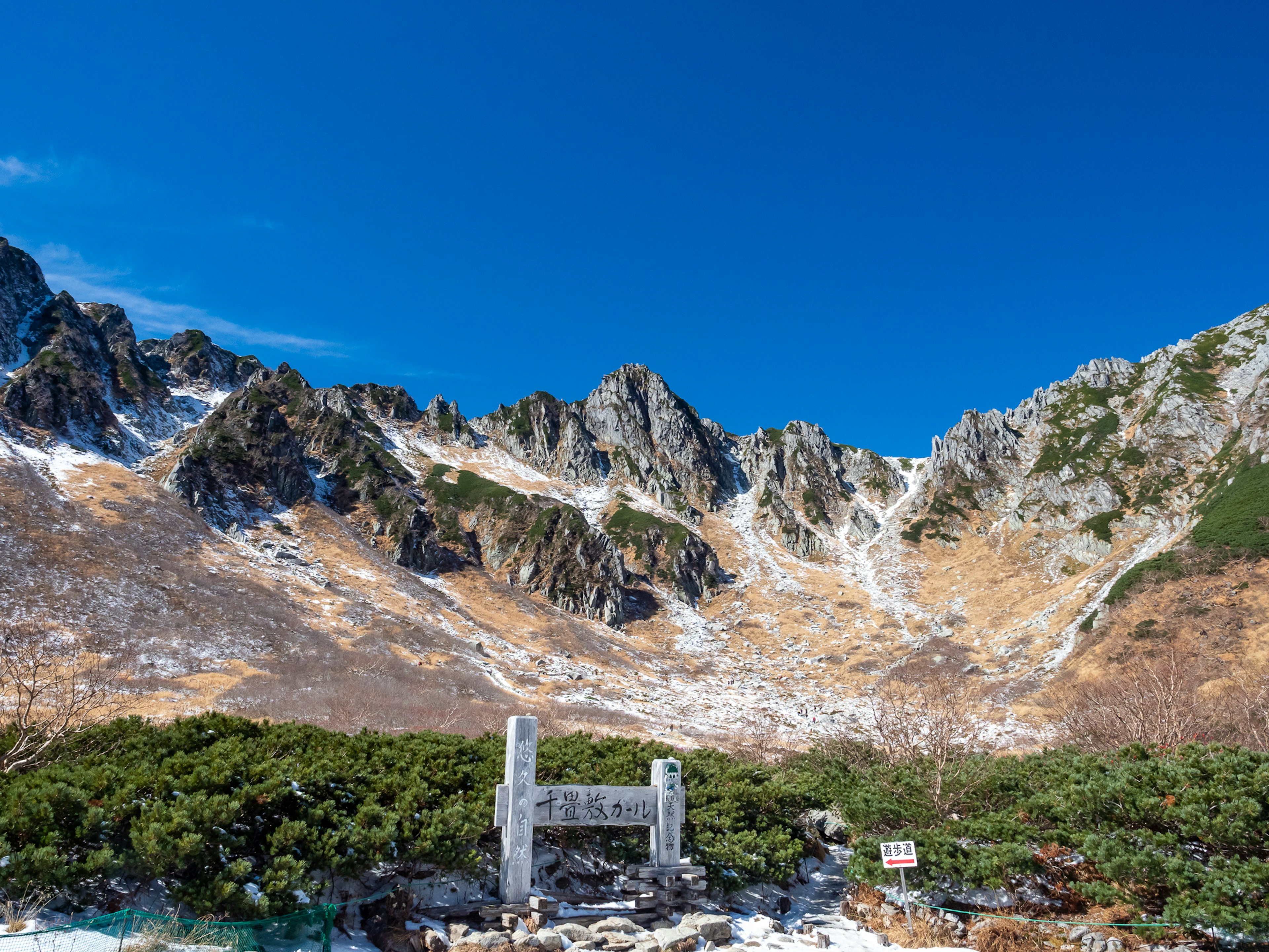 Puerta de piedra bajo un cielo azul claro con majestuosas montañas al fondo