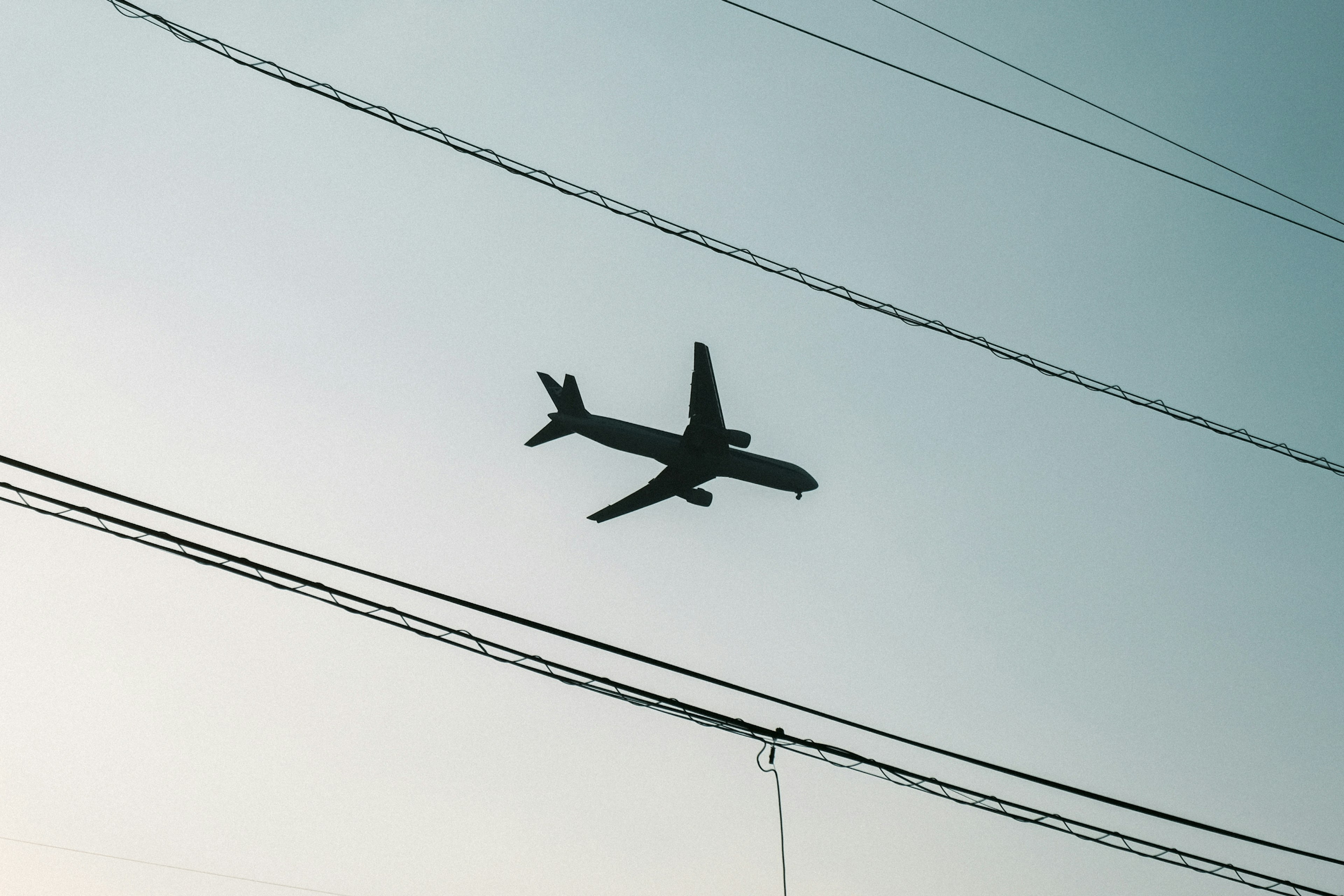 Silhouette d'un avion volant contre un ciel pâle avec des lignes électriques