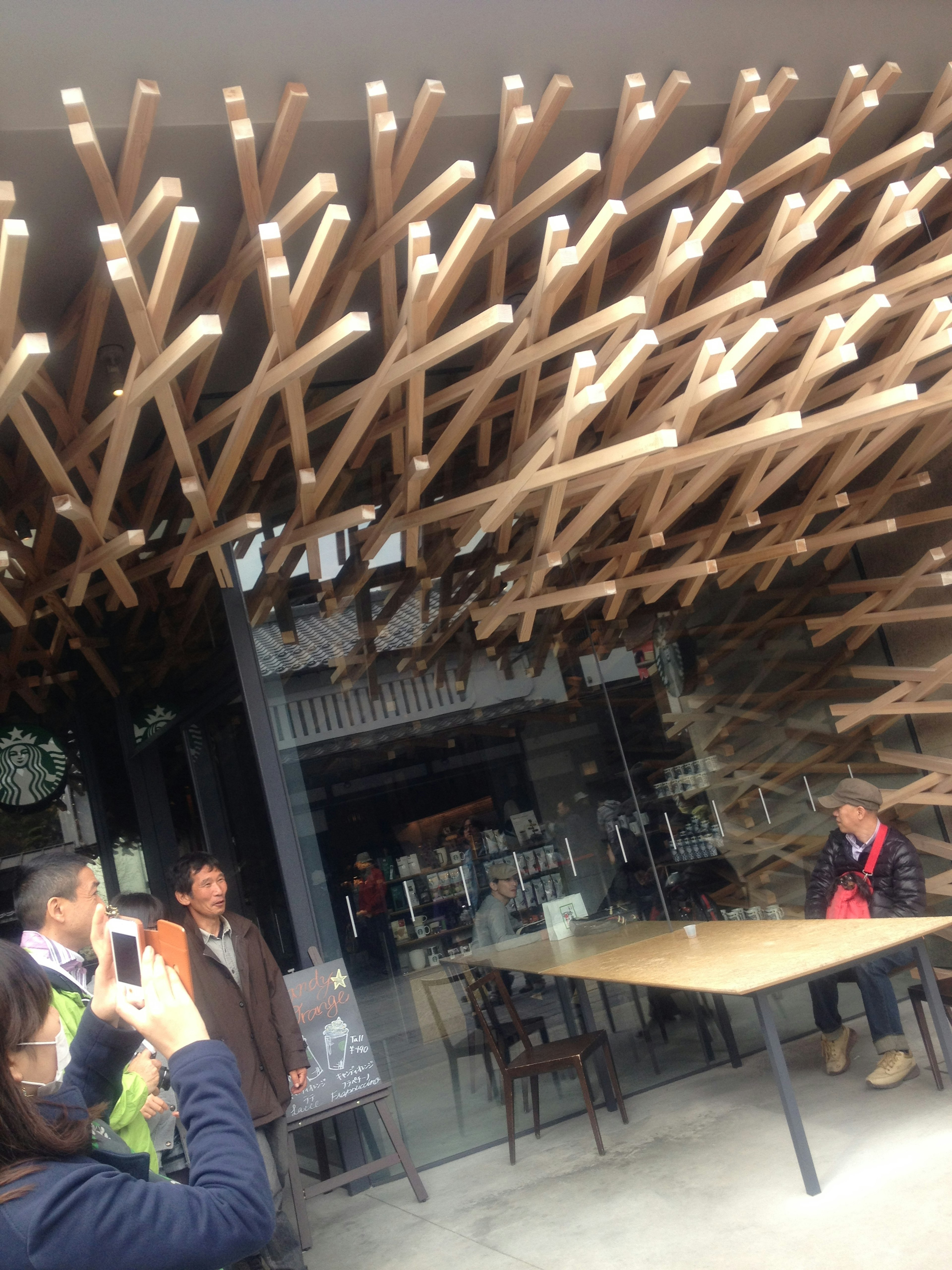 People in front of a cafe with a distinctive wooden art structure overhead