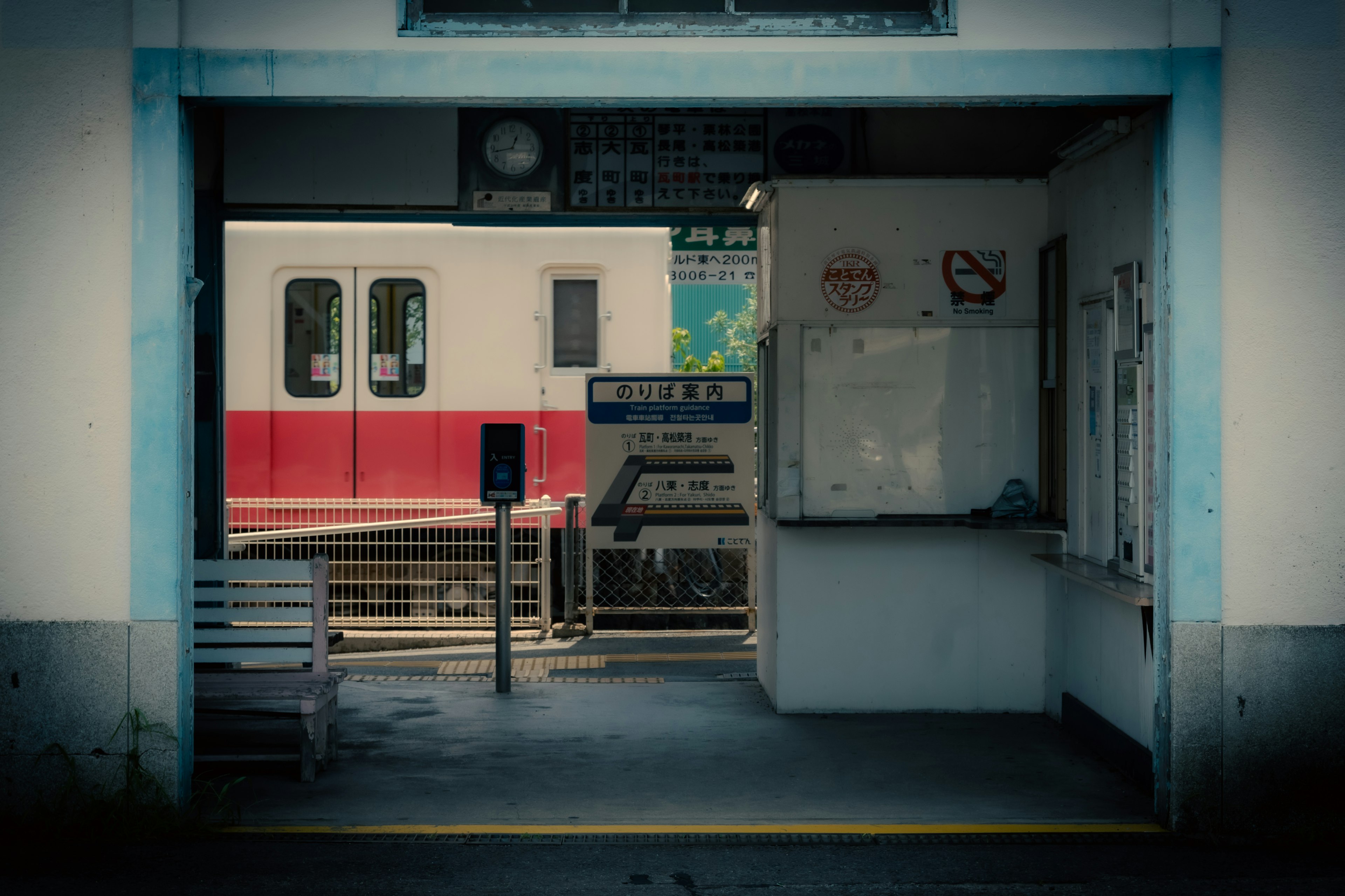 Blick auf einen roten Zug und ein Informationsschild vom Eingang eines Bahnhofs