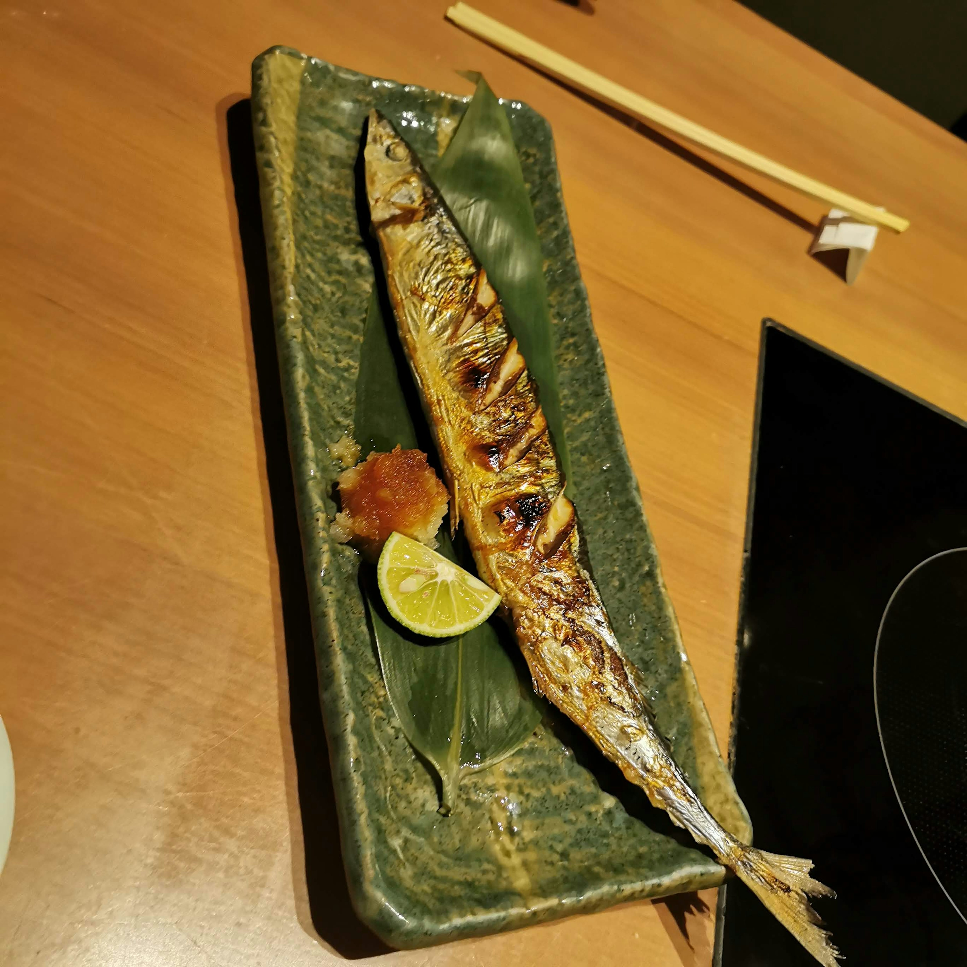 Poisson sanma grillé présenté sur une assiette verte avec du citron et des garnitures