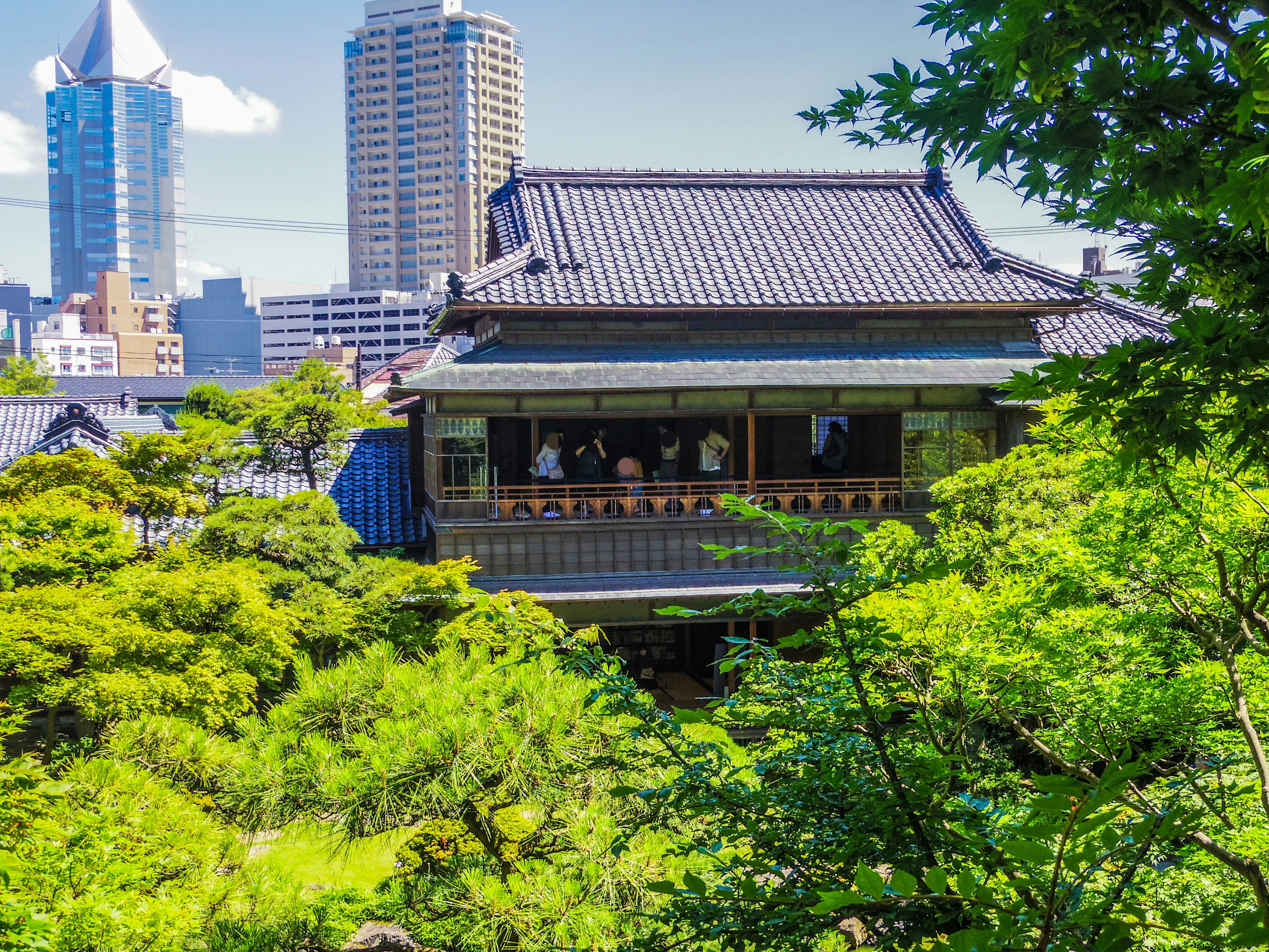 Maison japonaise traditionnelle entourée de verdure avec des gratte-ciel modernes en arrière-plan