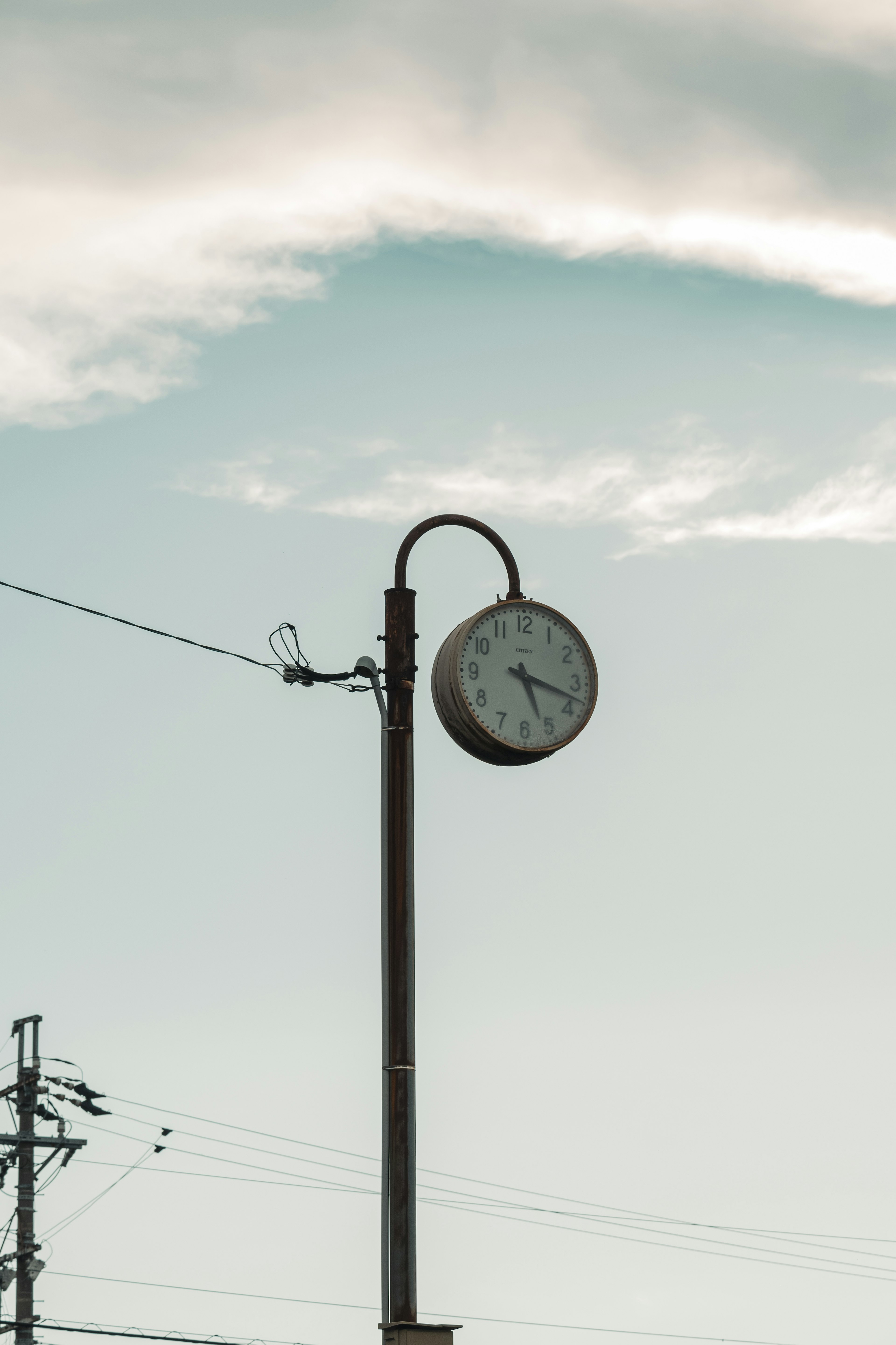 Analoge Uhr, die unter einem blauen Himmel an einer Straßenlaterne montiert ist