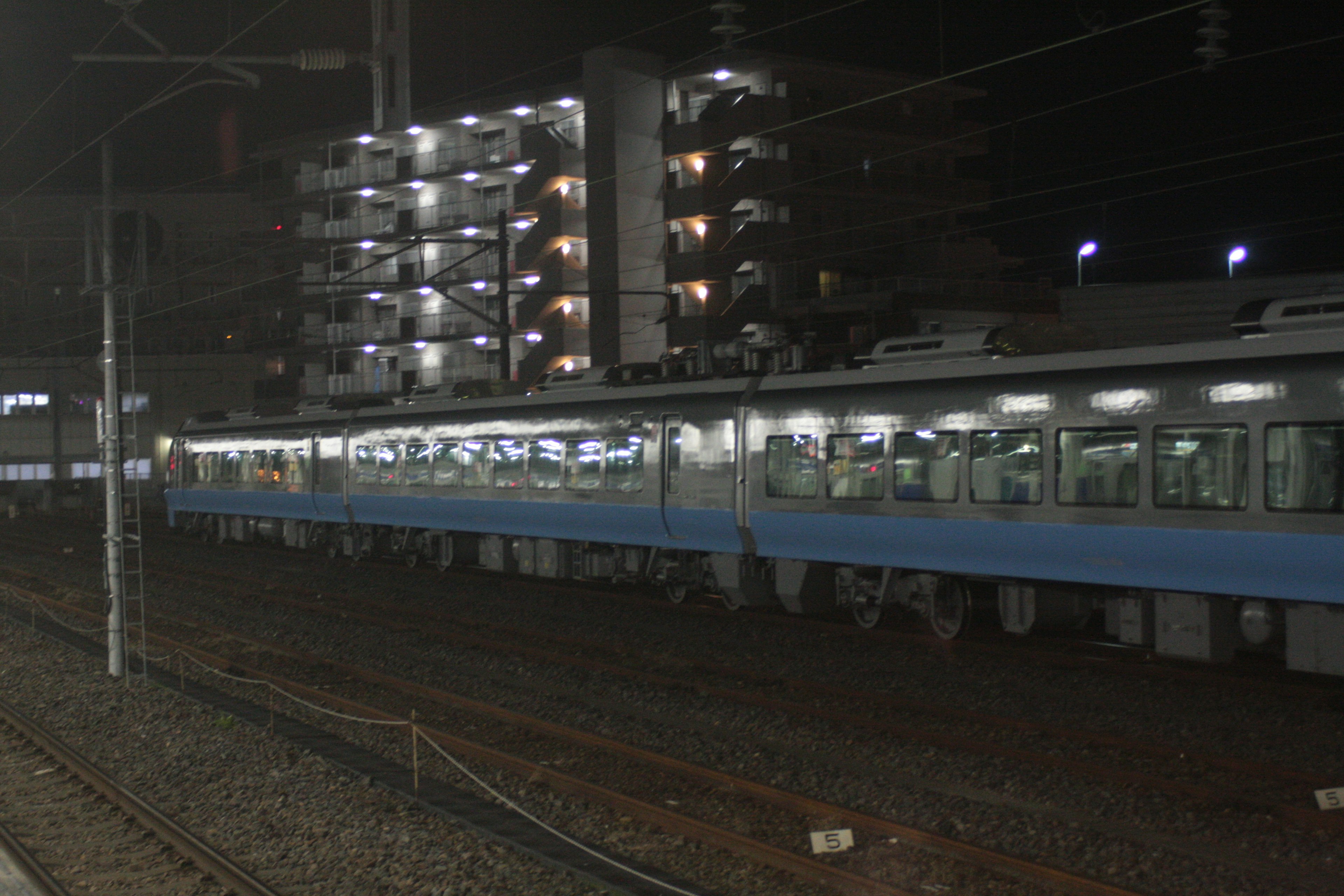 รถไฟสีน้ำเงินในเวลากลางคืนพร้อมอาคารที่สว่างอยู่ด้านหลัง