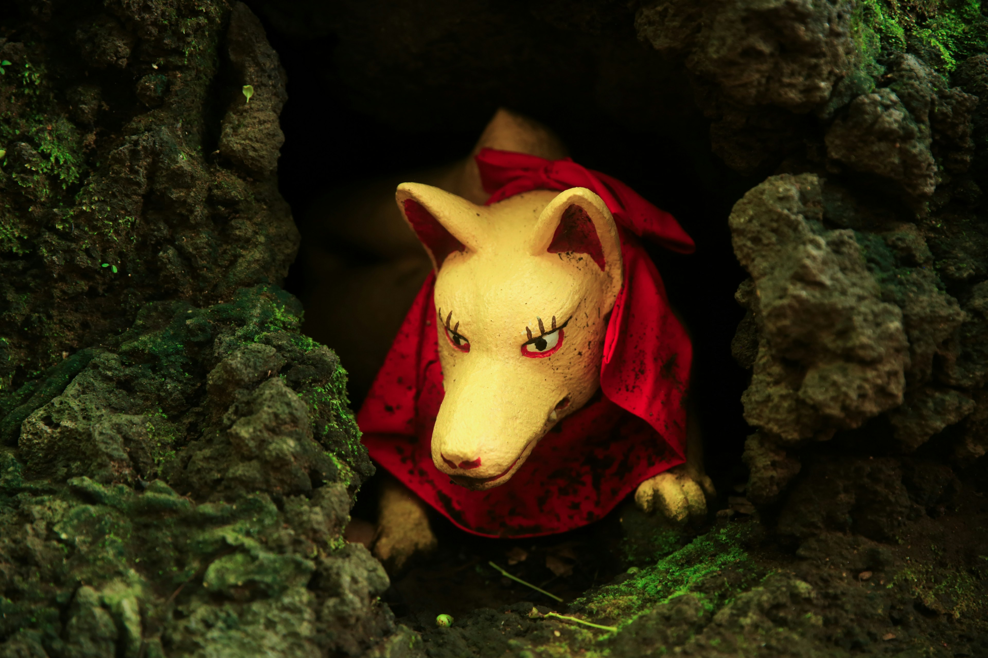 A white stuffed dog wearing a red cloak peeking out from a cave