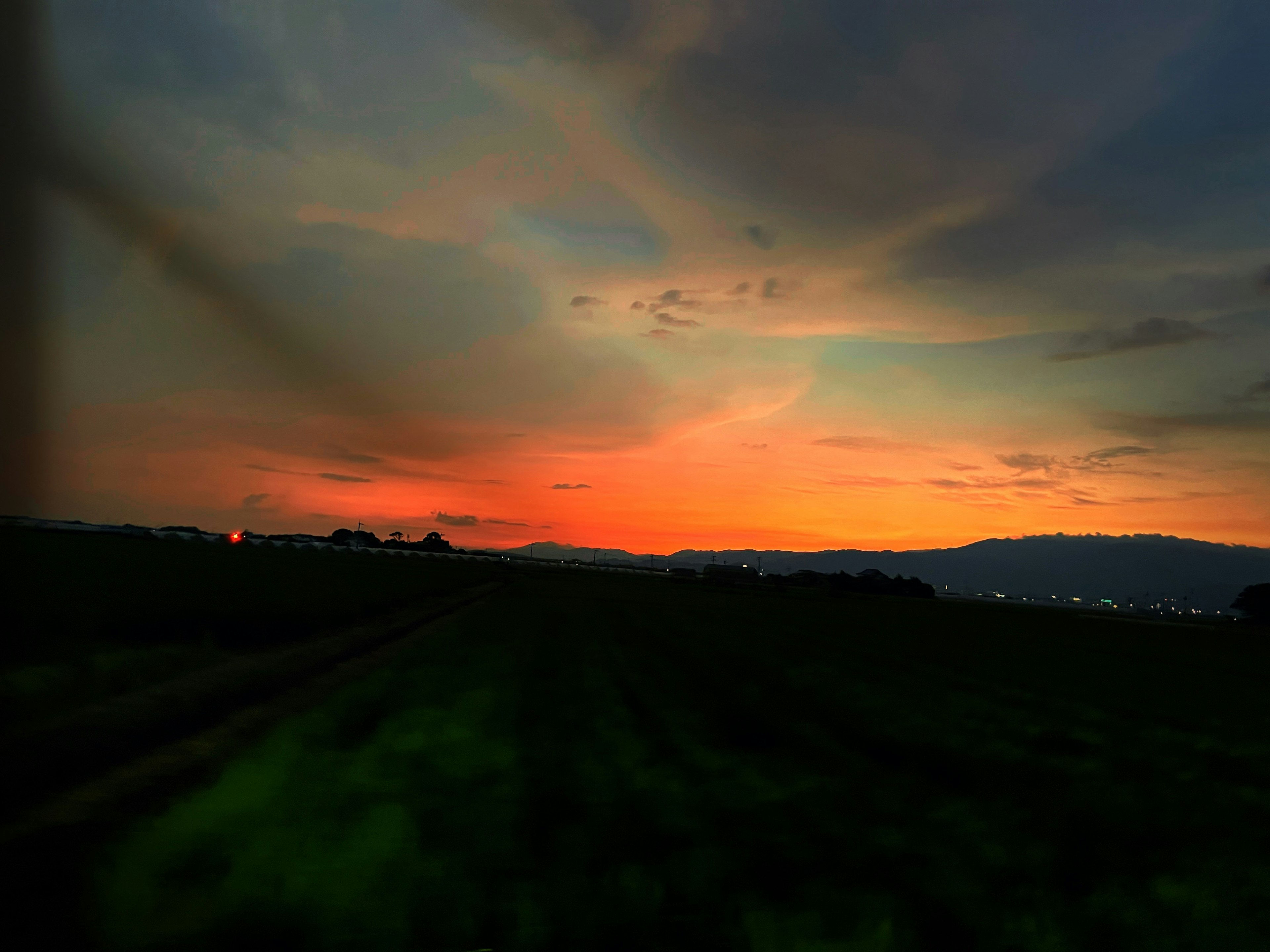 Cielo de atardecer vibrante con nubes sobre colinas distantes y luces de la ciudad