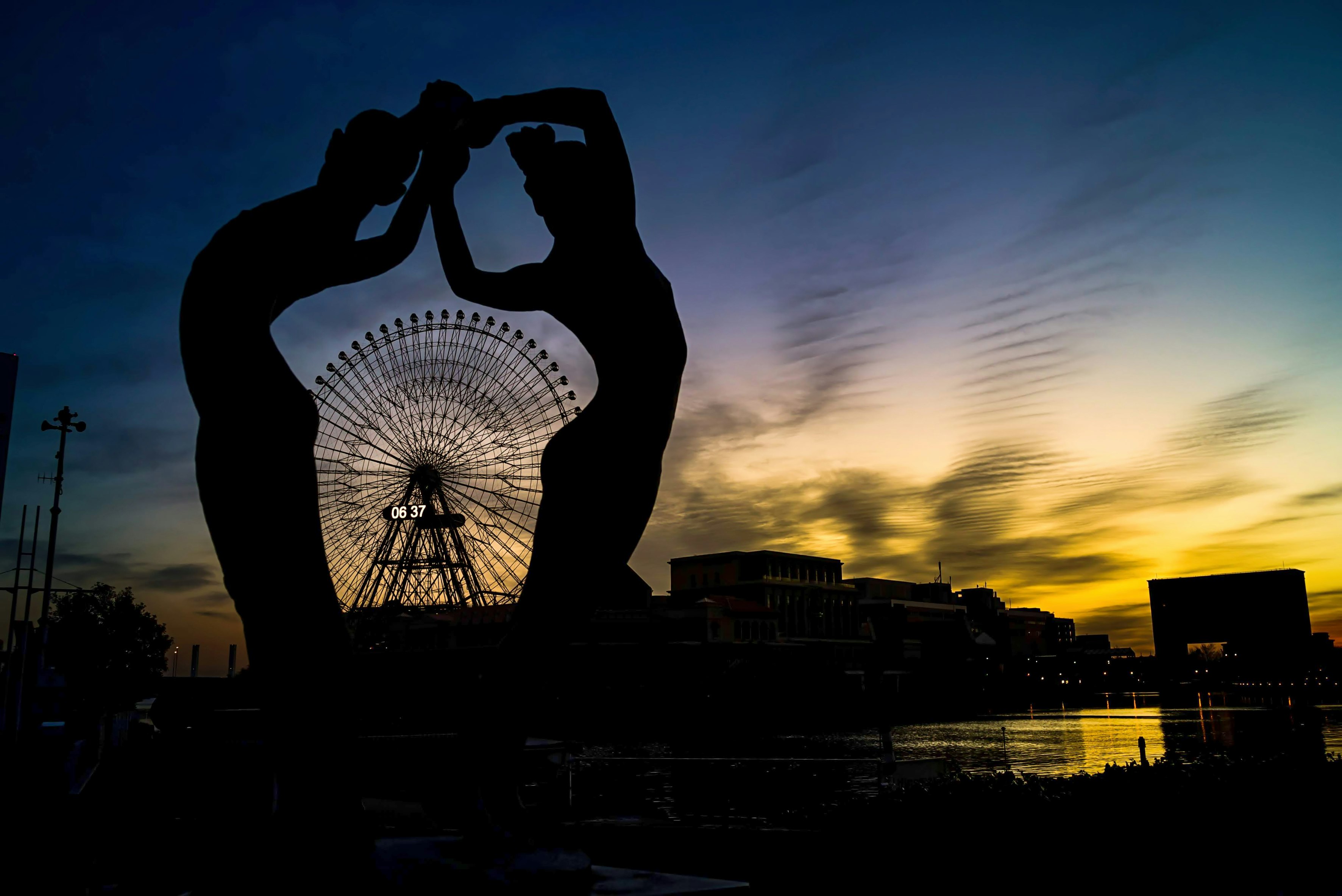 Silhouette von zwei Figuren vor einem Sonnenuntergang mit einem Riesenrad
