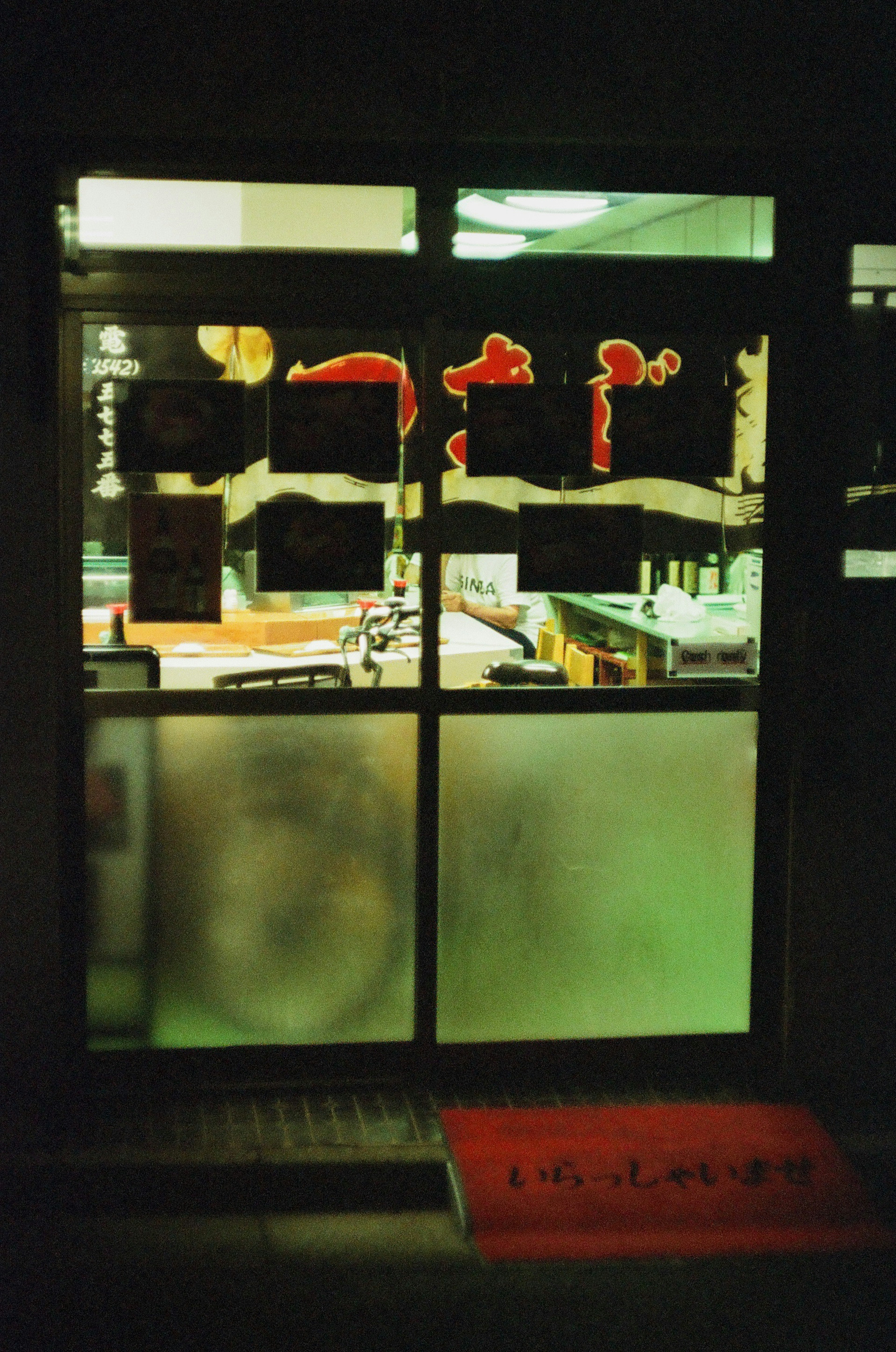 Restaurantfenster mit rotem Schild und mattiertem Glas in einer dunklen Umgebung