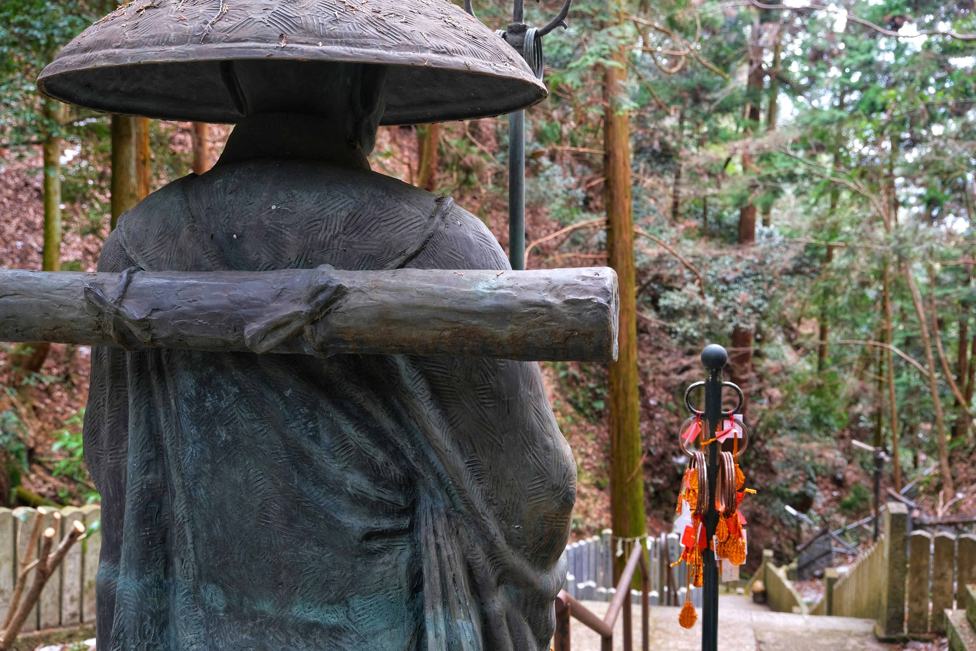 Vista posteriore di una statua di pietra in una foresta tranquilla che indossa un cappello e porta un tronco di legno sulla schiena