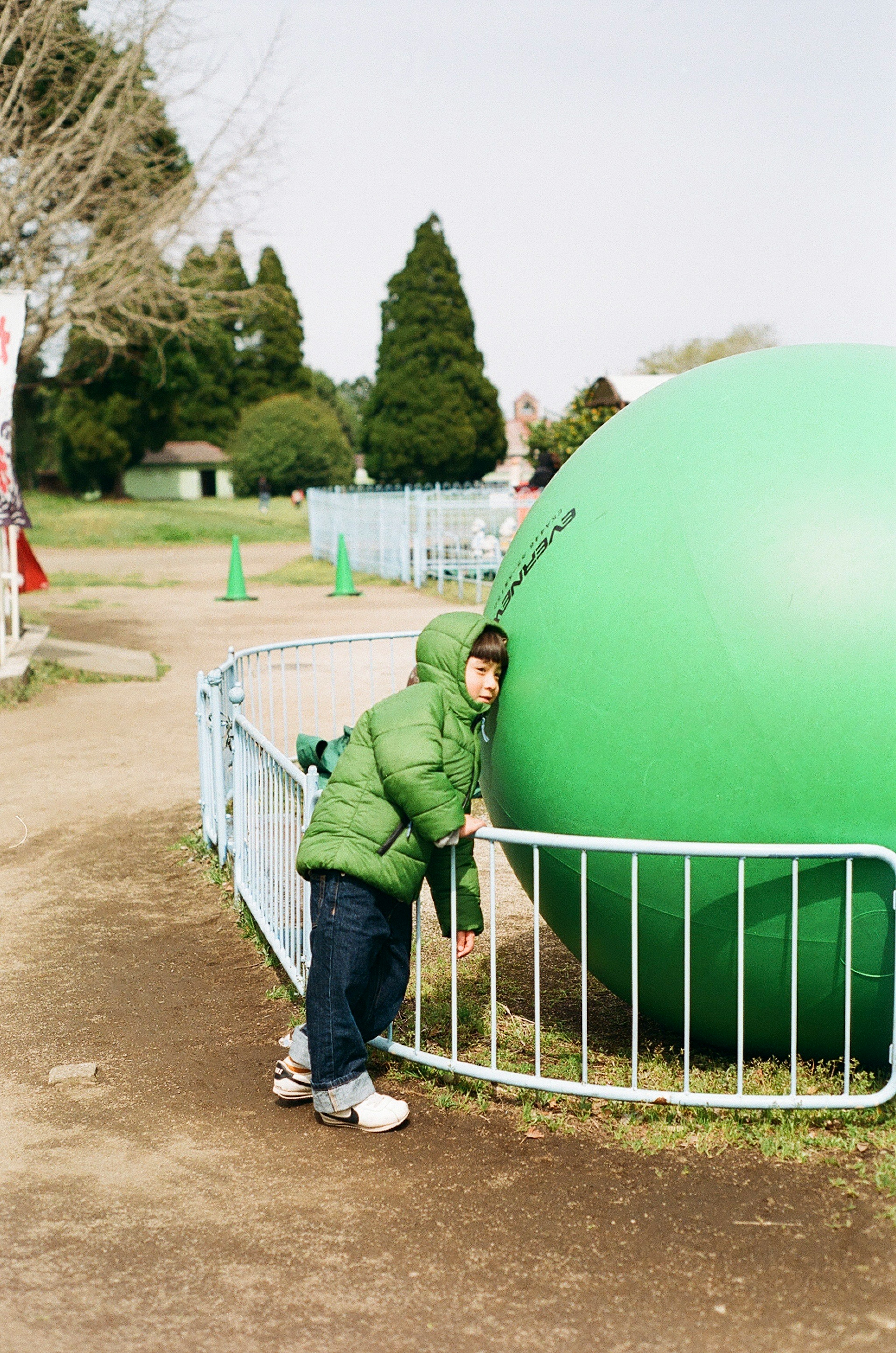 Child leaning against a large green ball in a park playground