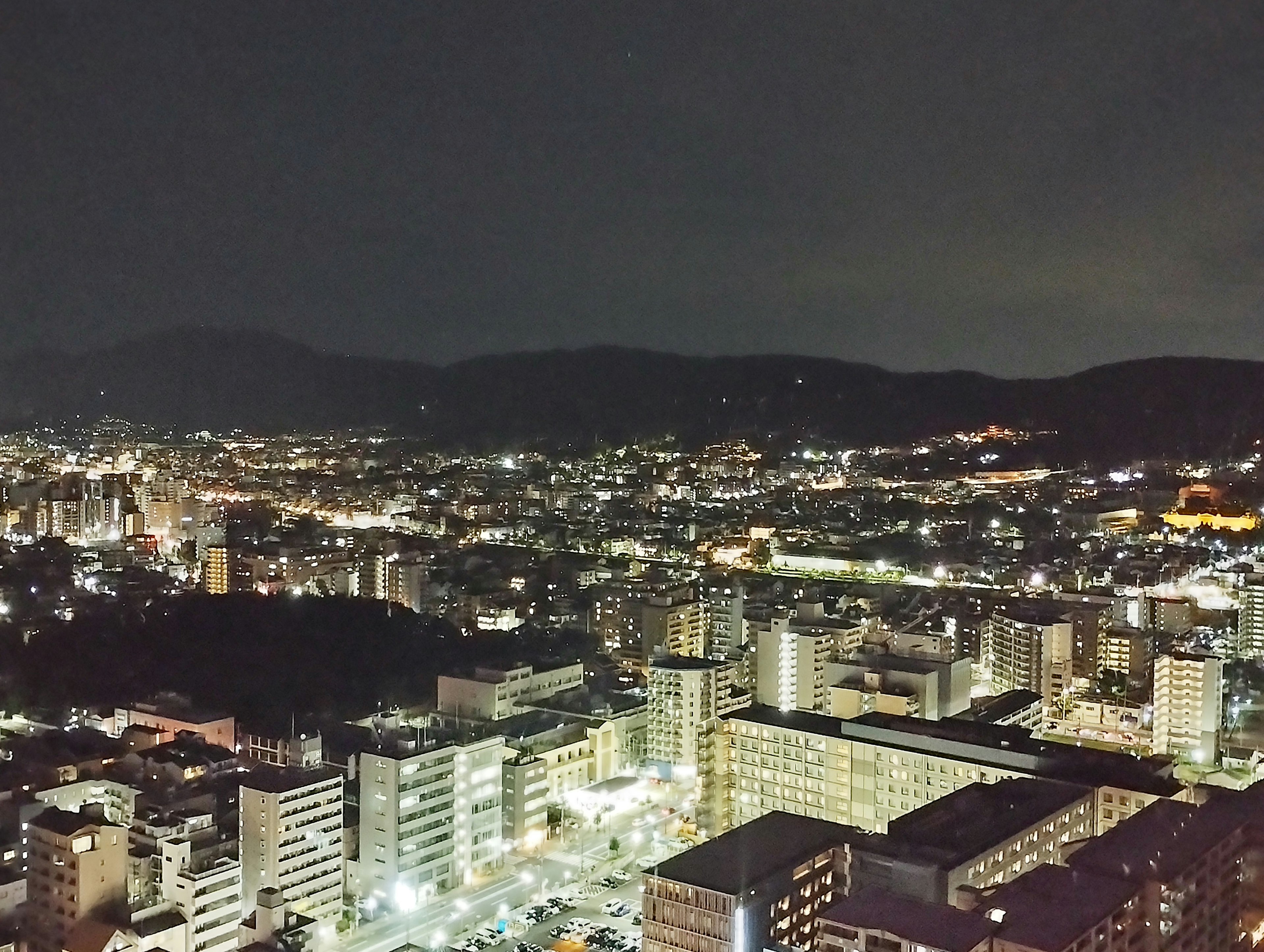 Panorama notturno della città con edifici illuminati e montagne