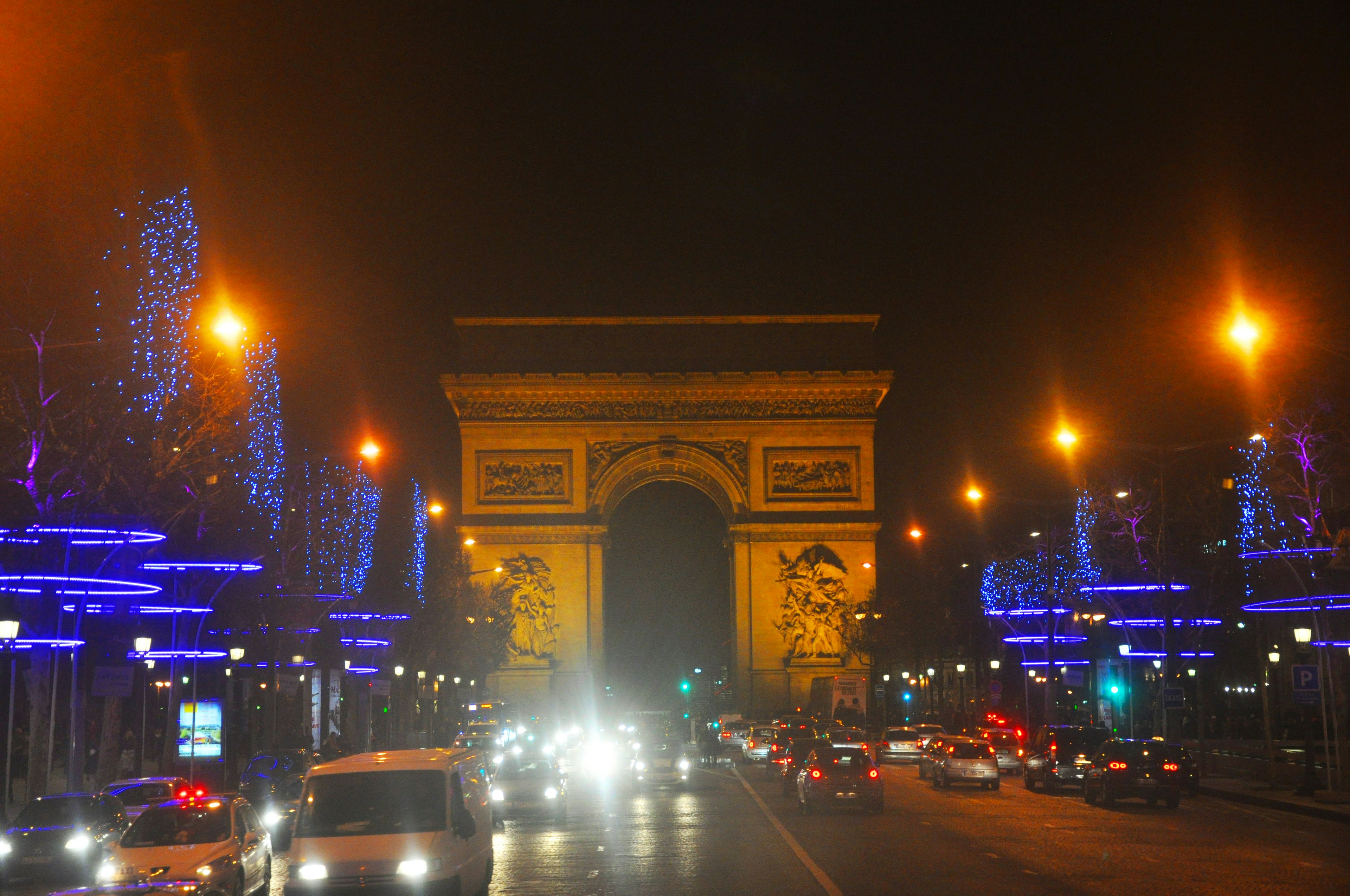 Arc de Triomphe yang diterangi di malam hari dengan lampu perayaan di jalan