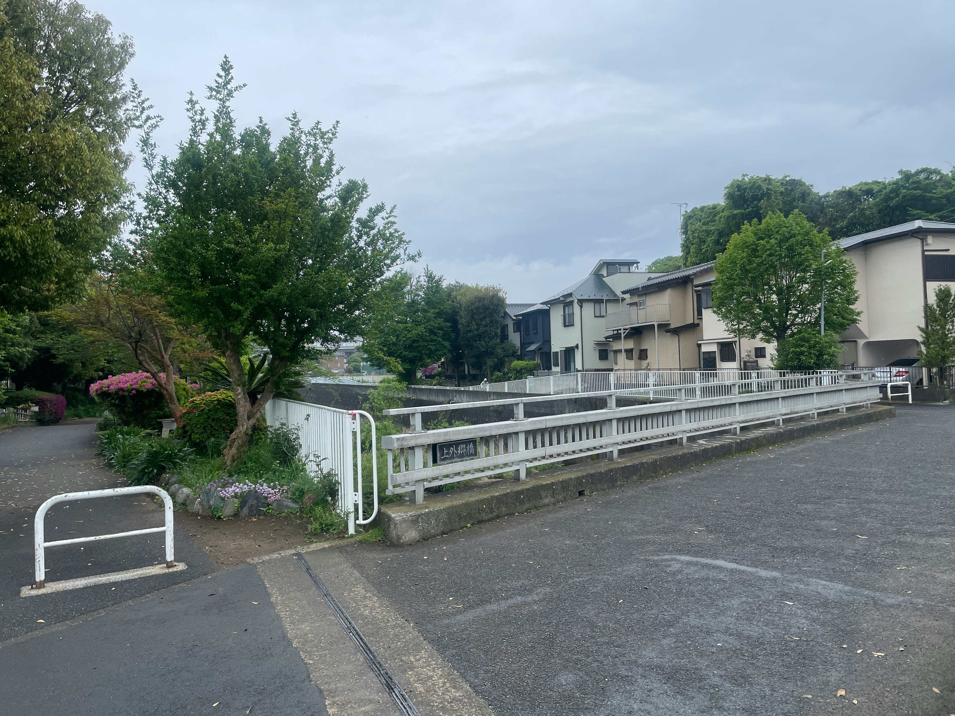 View of a park with green trees and a white fence alongside residential buildings