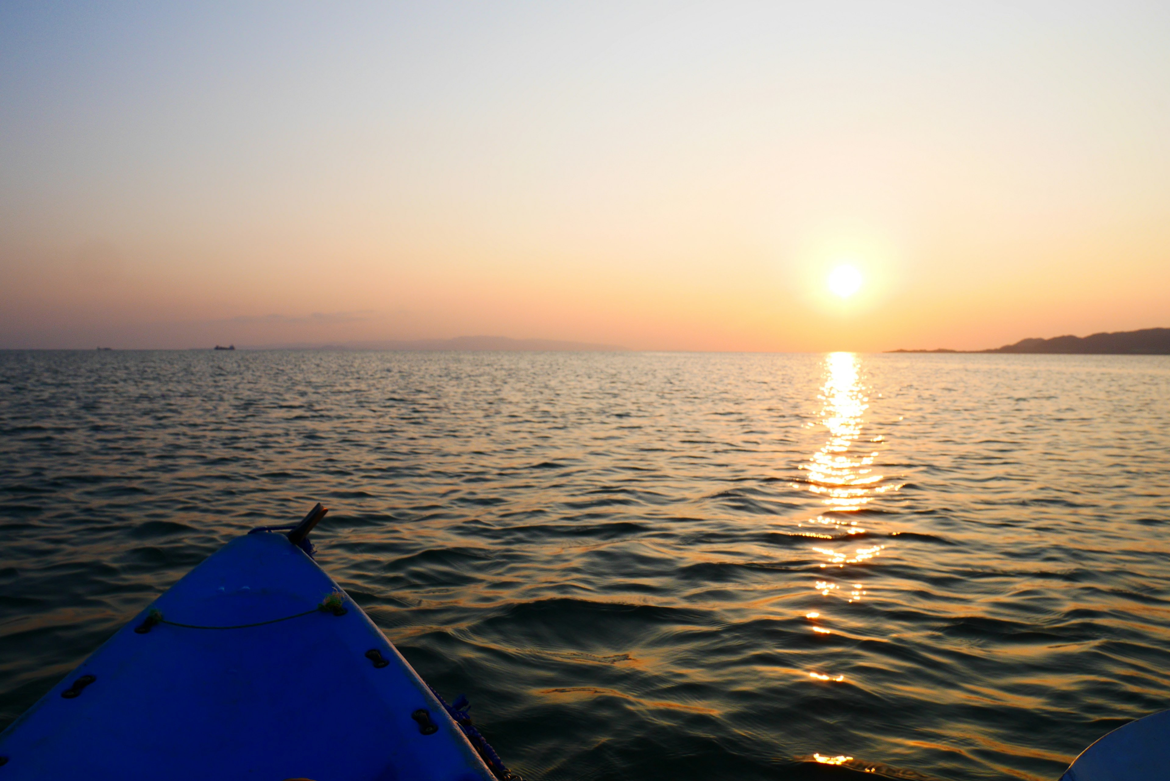 View of sunset and calm sea from the tip of a blue kayak