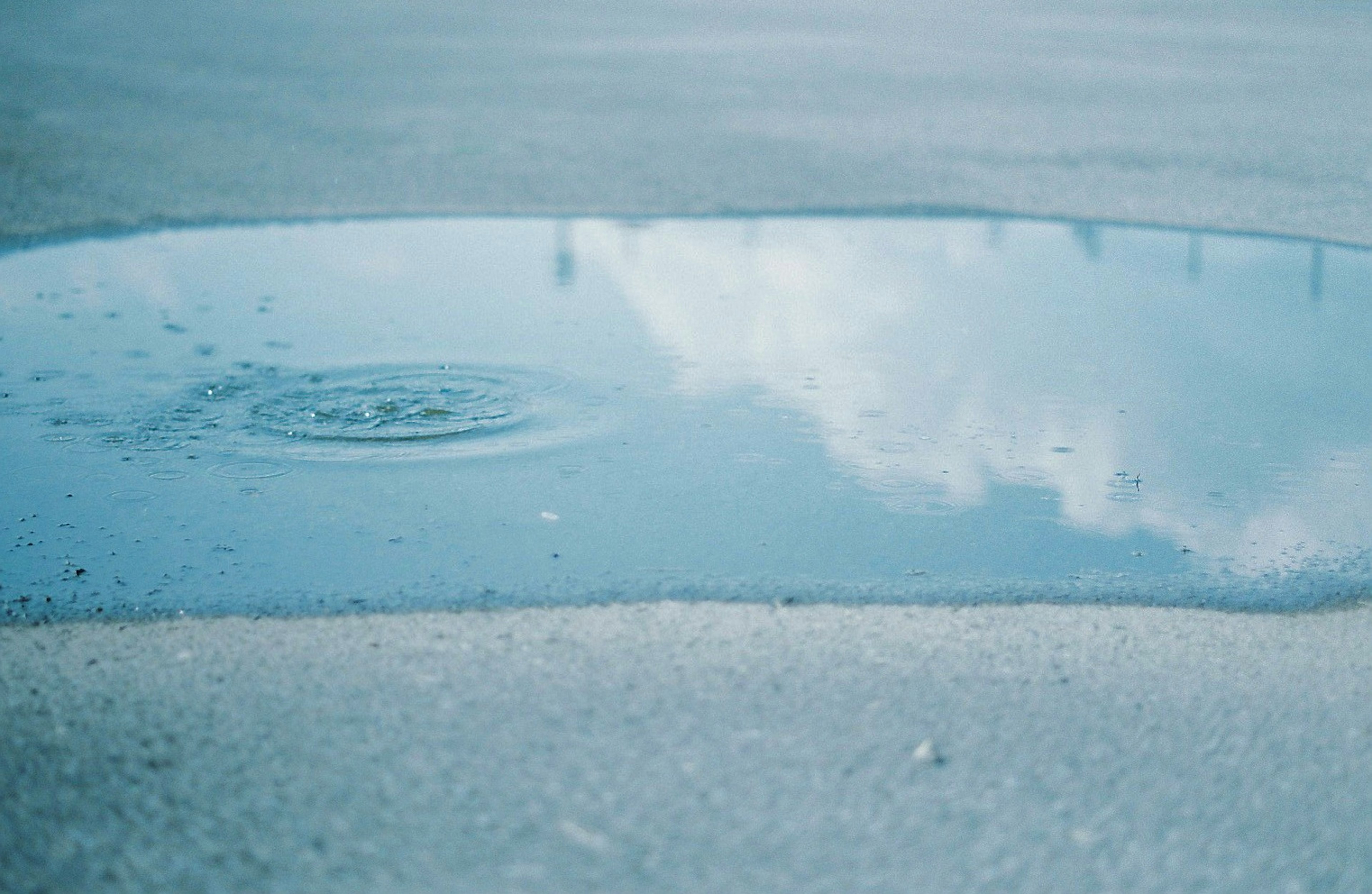 Puddle che riflette il cielo blu e le nuvole con onde