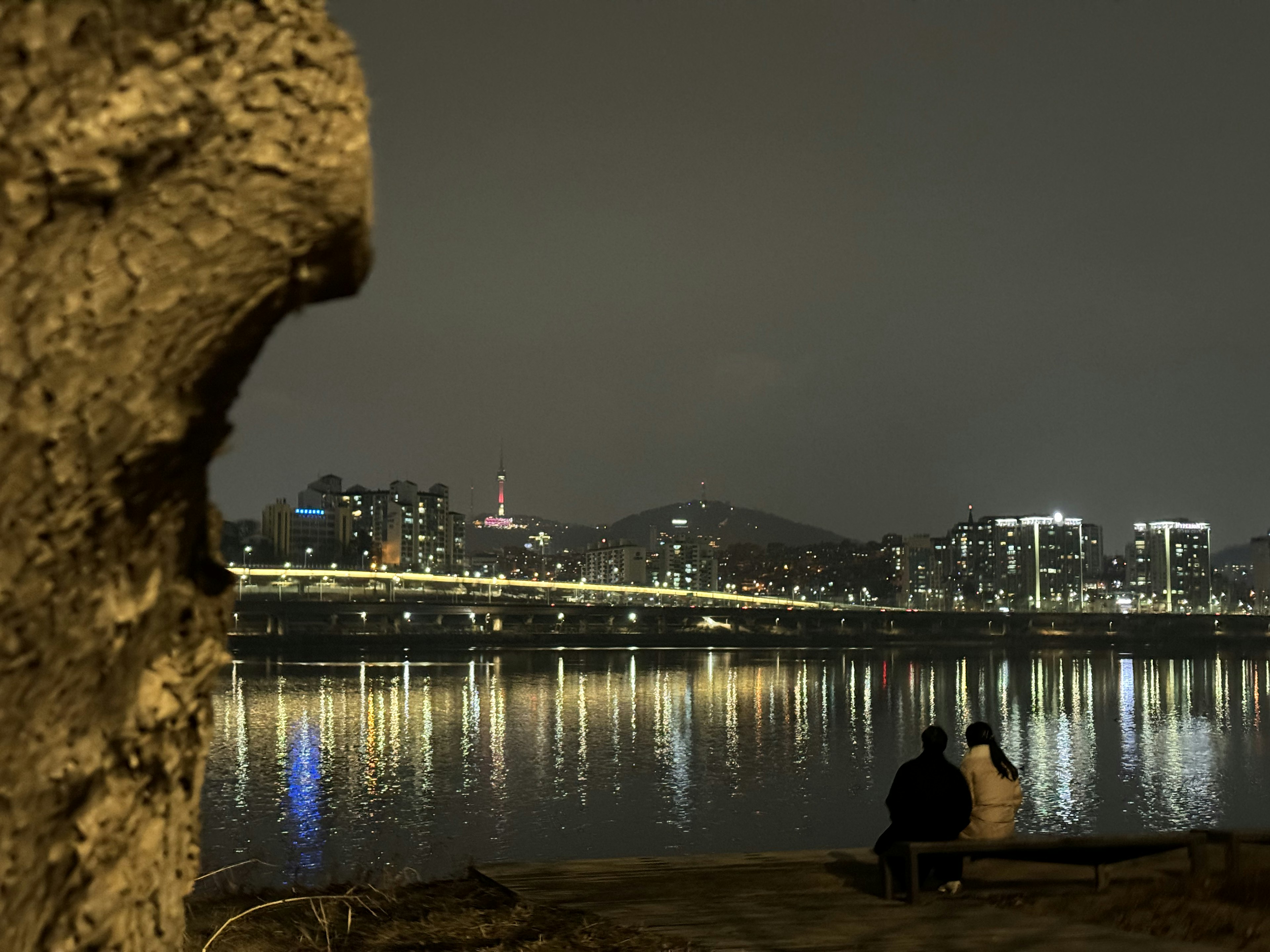 Vista nocturna del río Han con una pareja sentada junto al agua