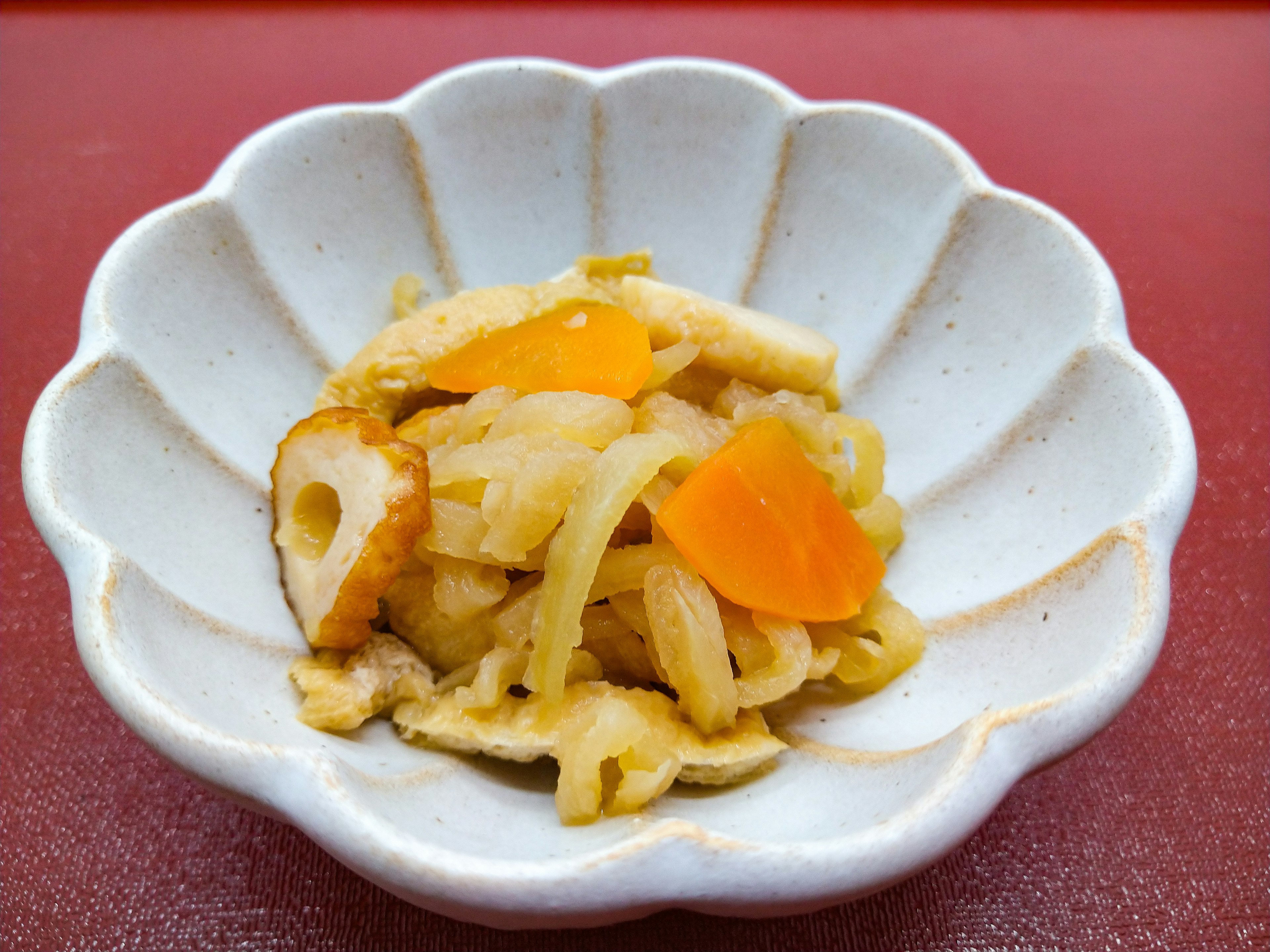 Japanese side dish served in a white petal-shaped bowl featuring ingredients like fish cake and radish