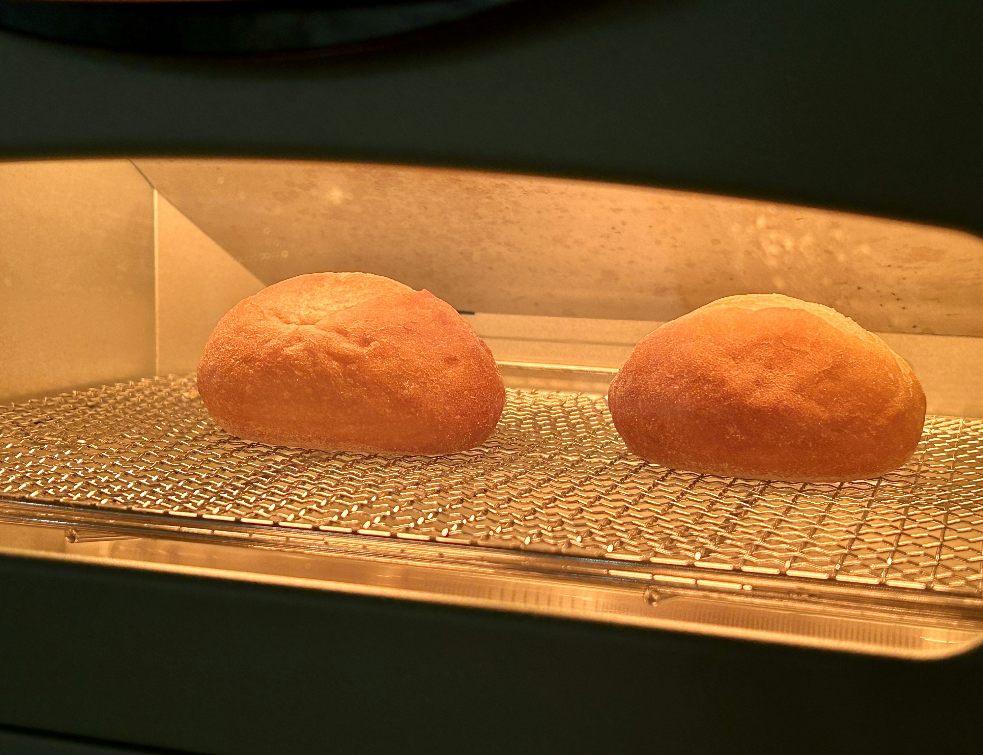 Two bread rolls baking in an oven with warm lighting