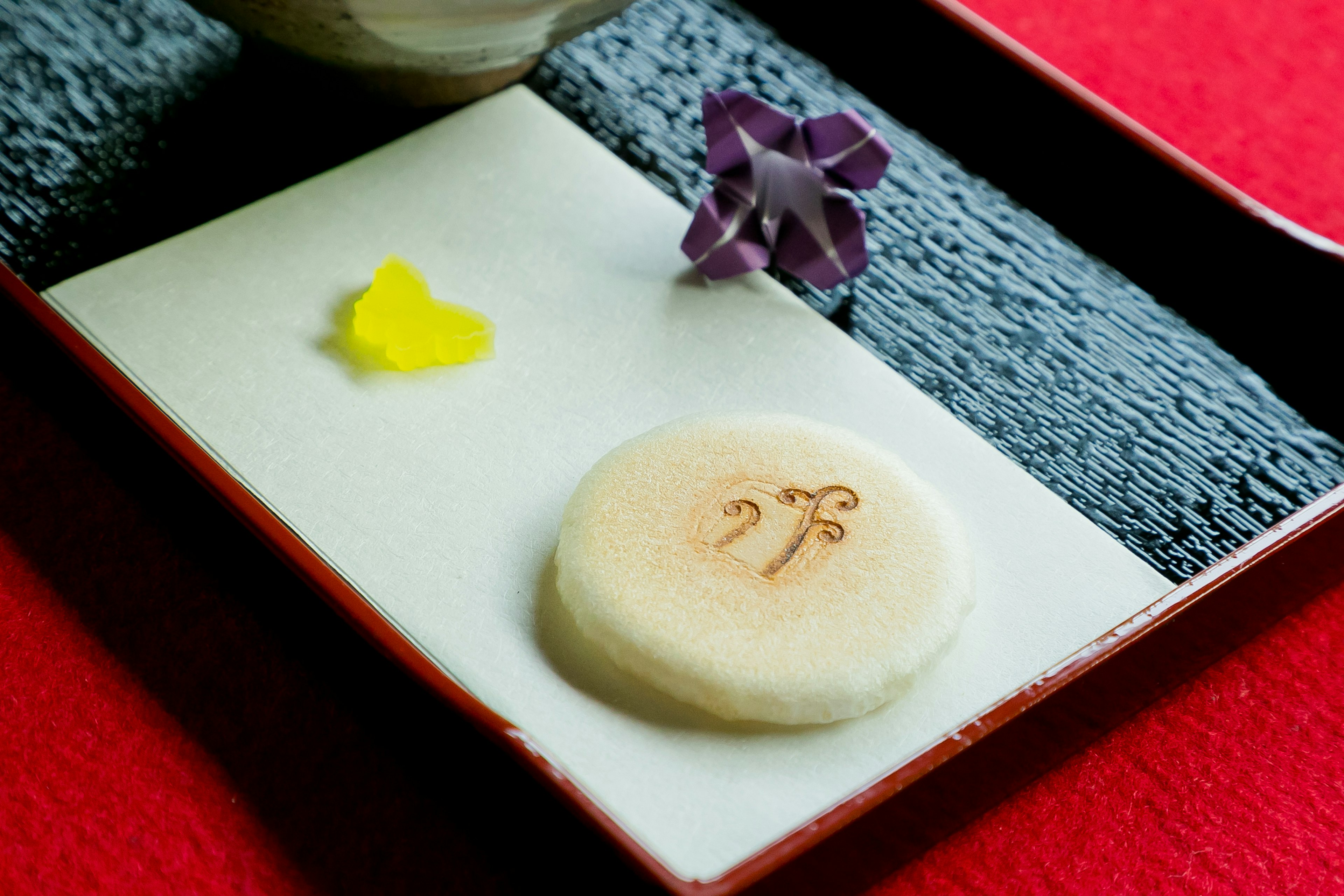 Schönes Teller mit japanischen Süßigkeiten und floraler Dekoration auf rotem Hintergrund