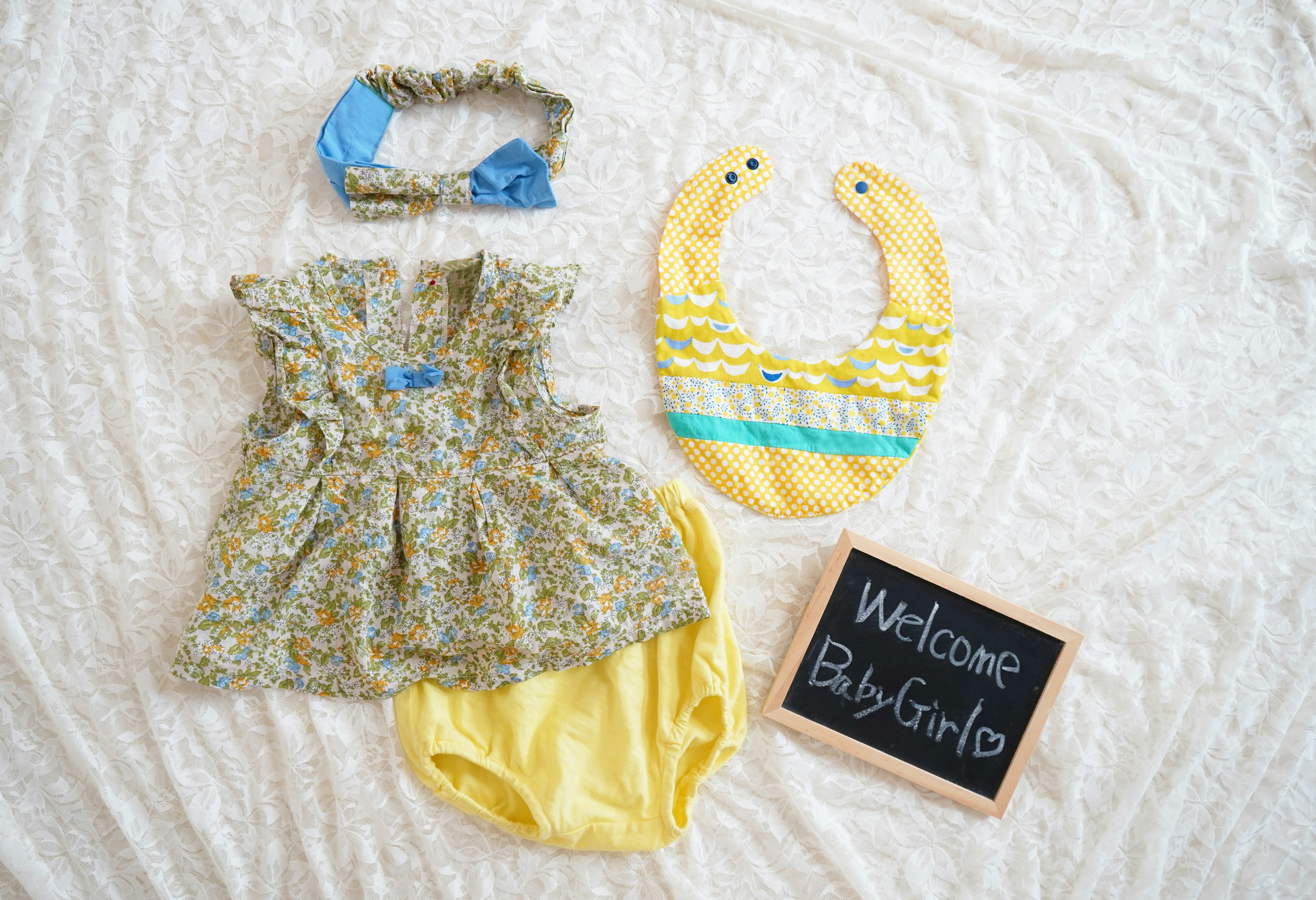 Image featuring a baby dress, bib, and headband with a chalkboard saying Welcome Baby Girl