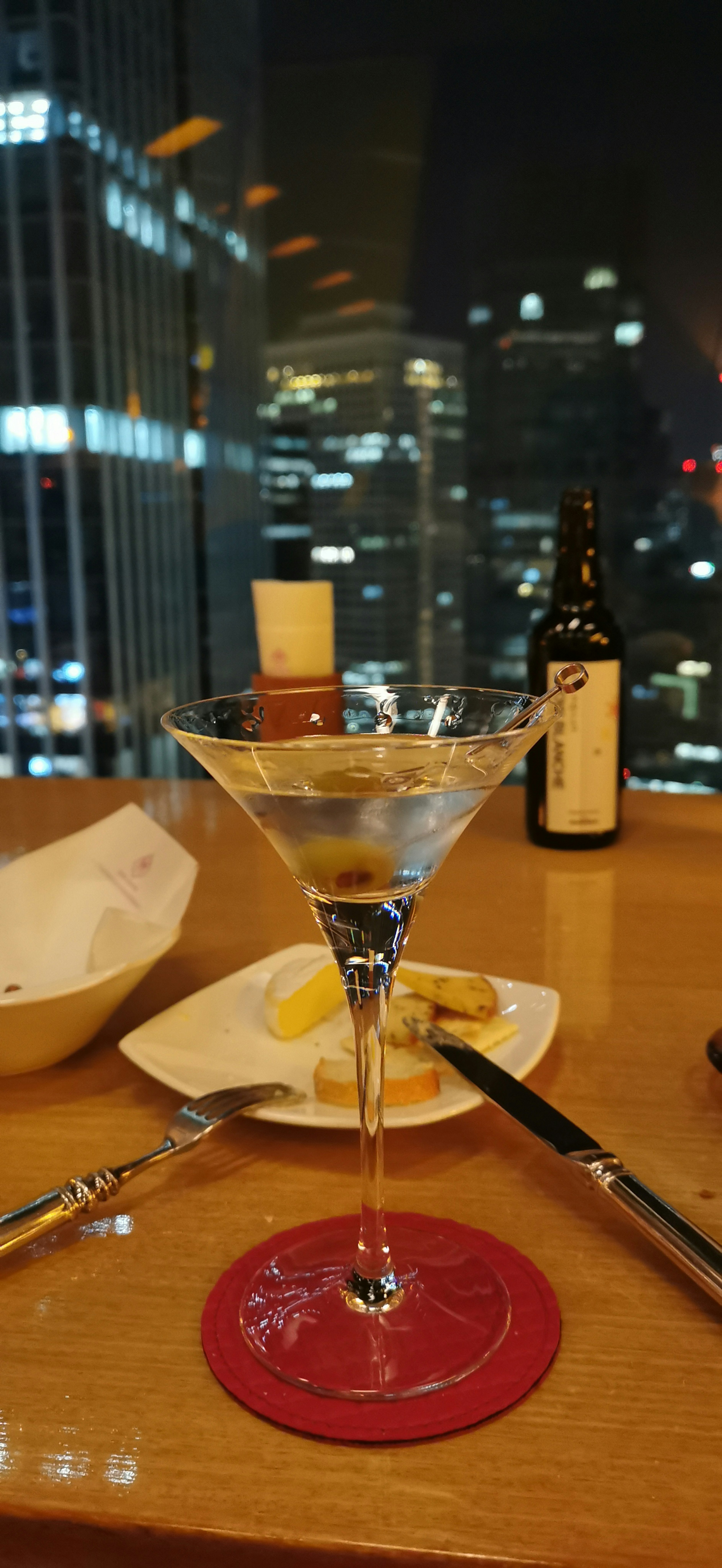 Copa de martini con vista de la ciudad de noche y elementos de comida