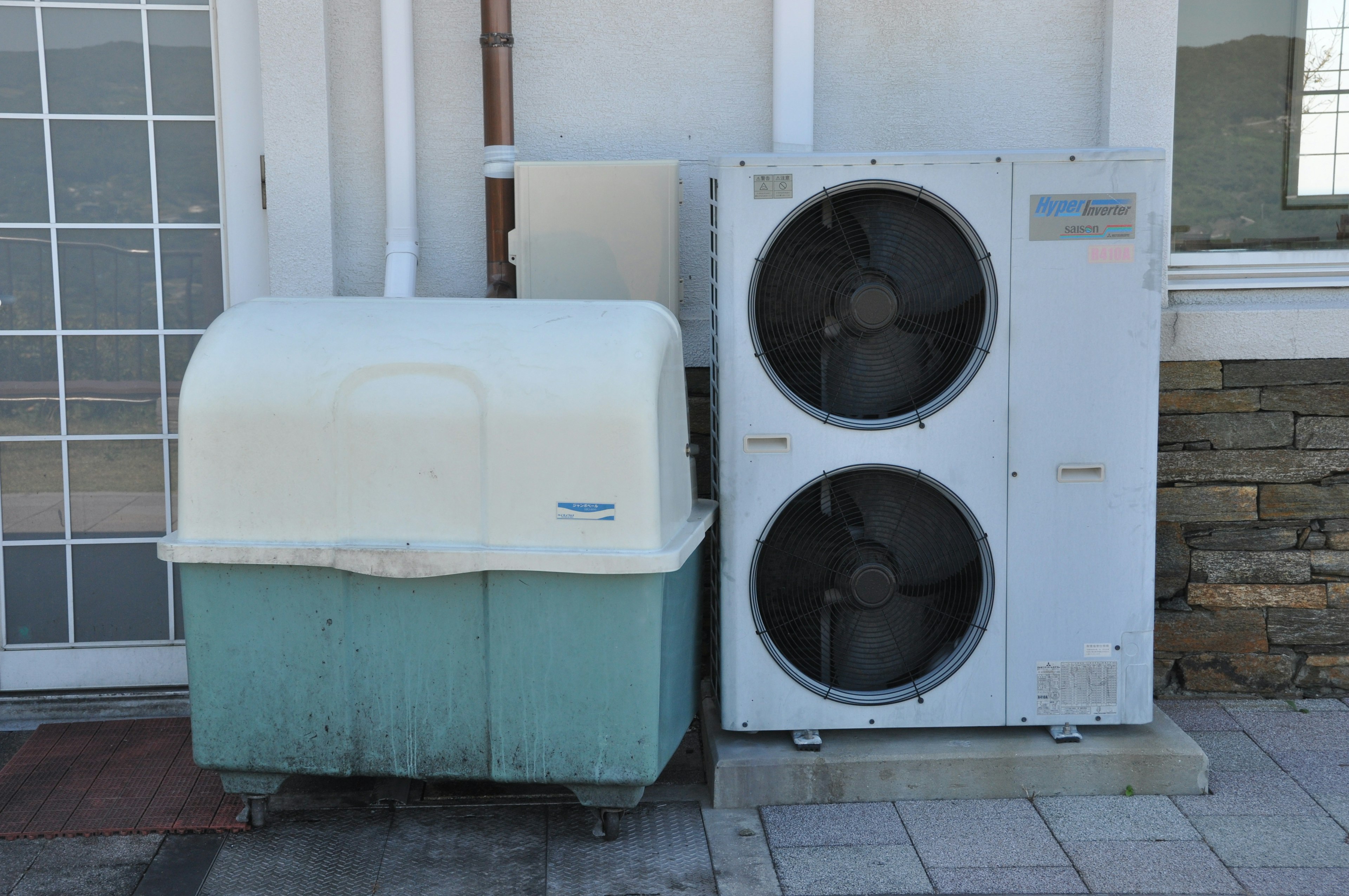 White air conditioning unit next to a light blue container against a wall