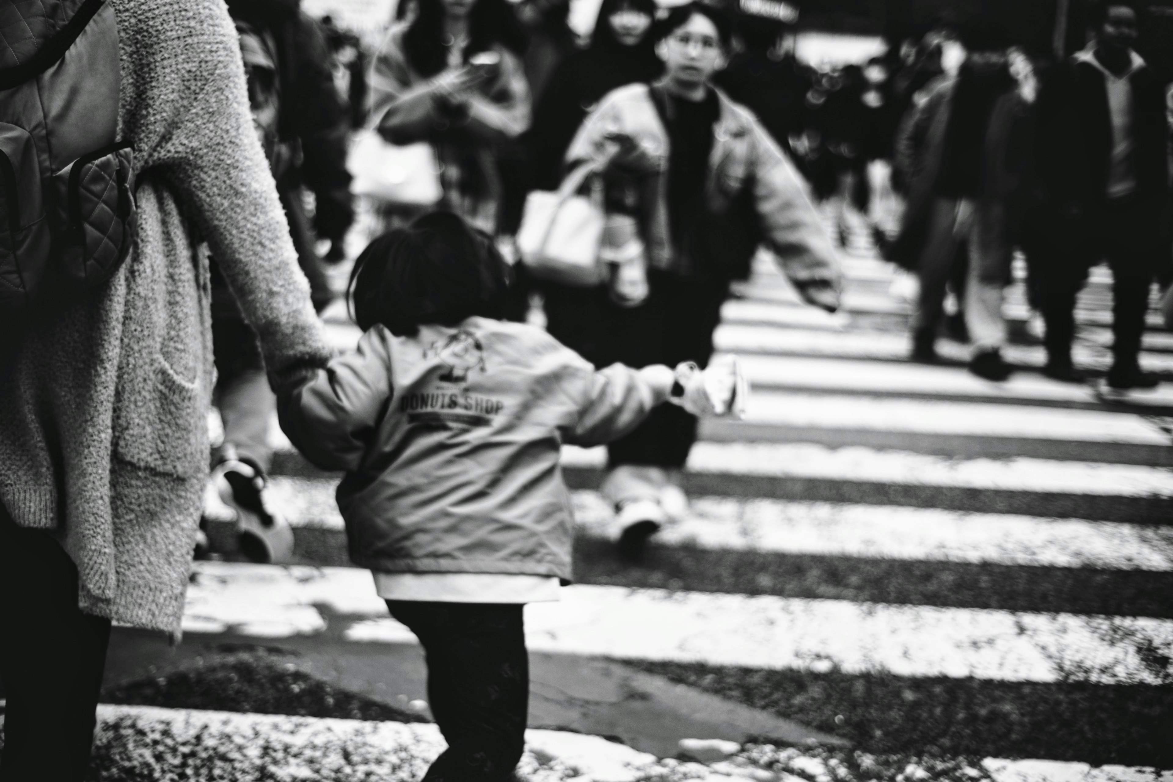 Black and white image of a child holding hands with an adult in a crosswalk