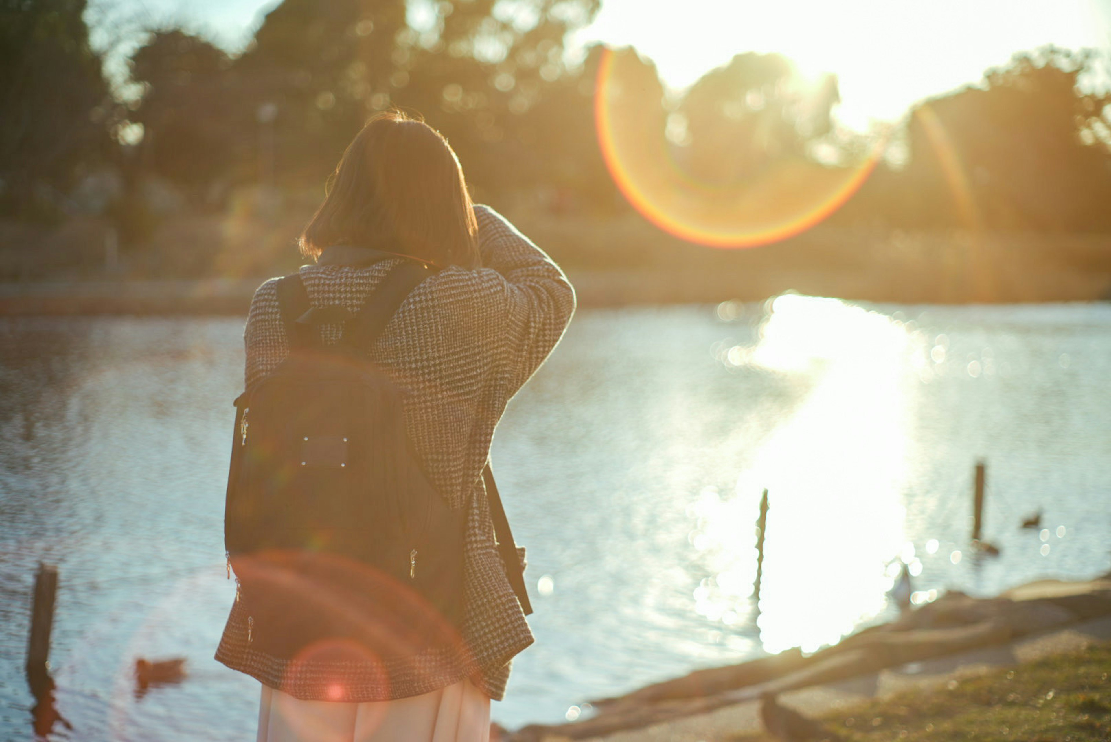 Donna con uno zaino che scatta foto a un lago al tramonto