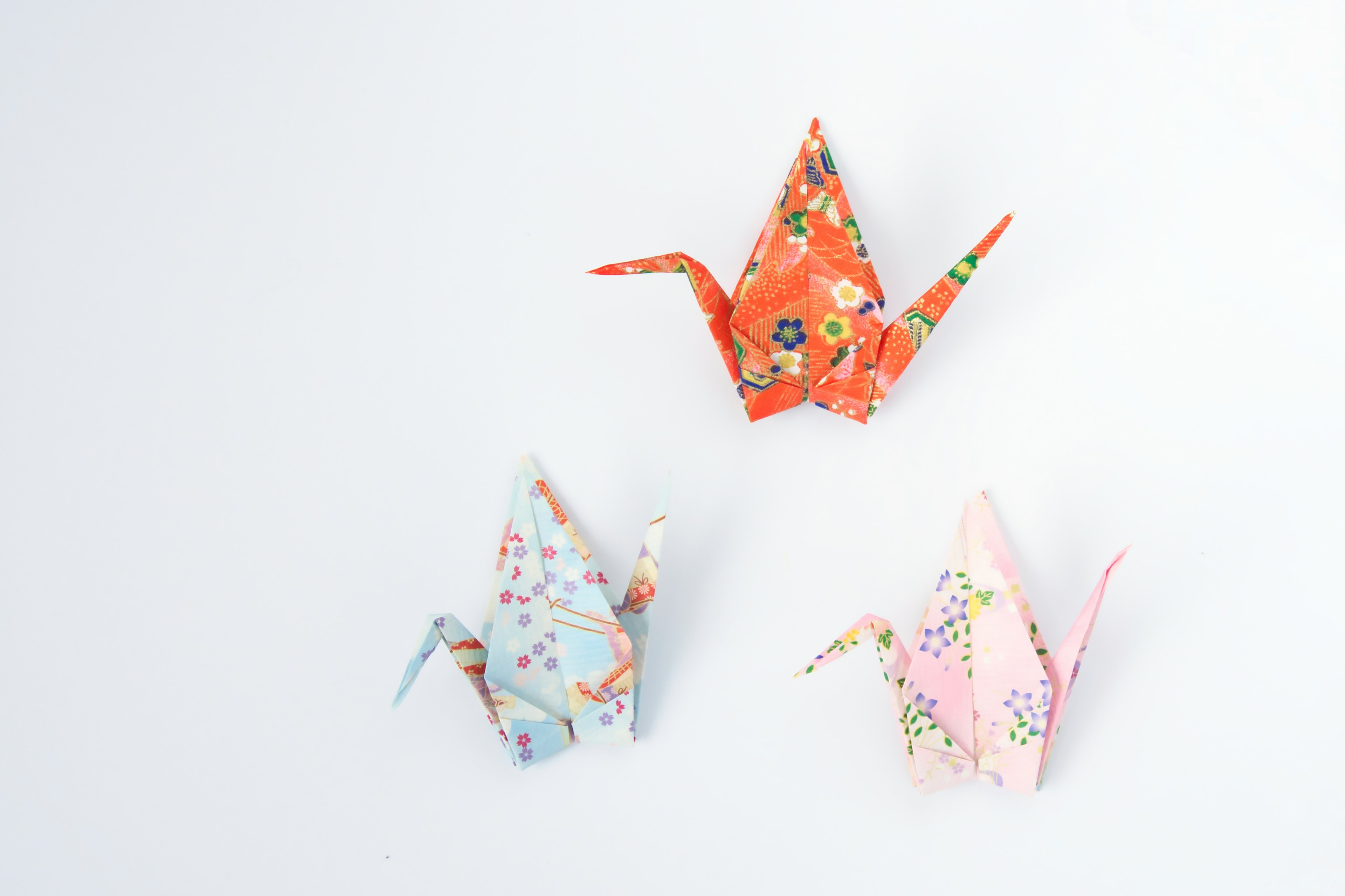 Tres grúas de origami coloridas dispuestas sobre un fondo simple