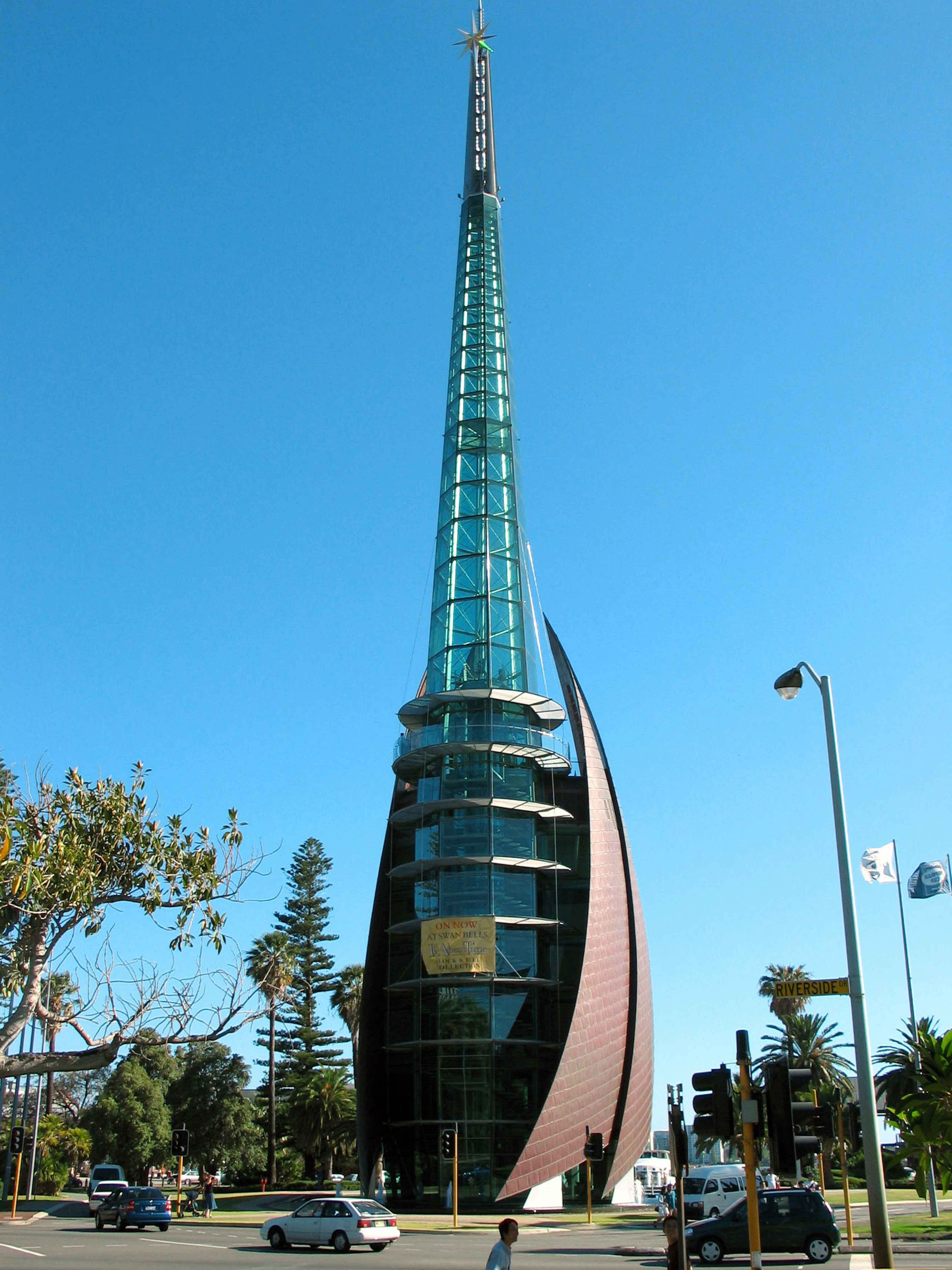 Torre moderna con diseño de vidrio y metal bajo un cielo azul rodeada de árboles