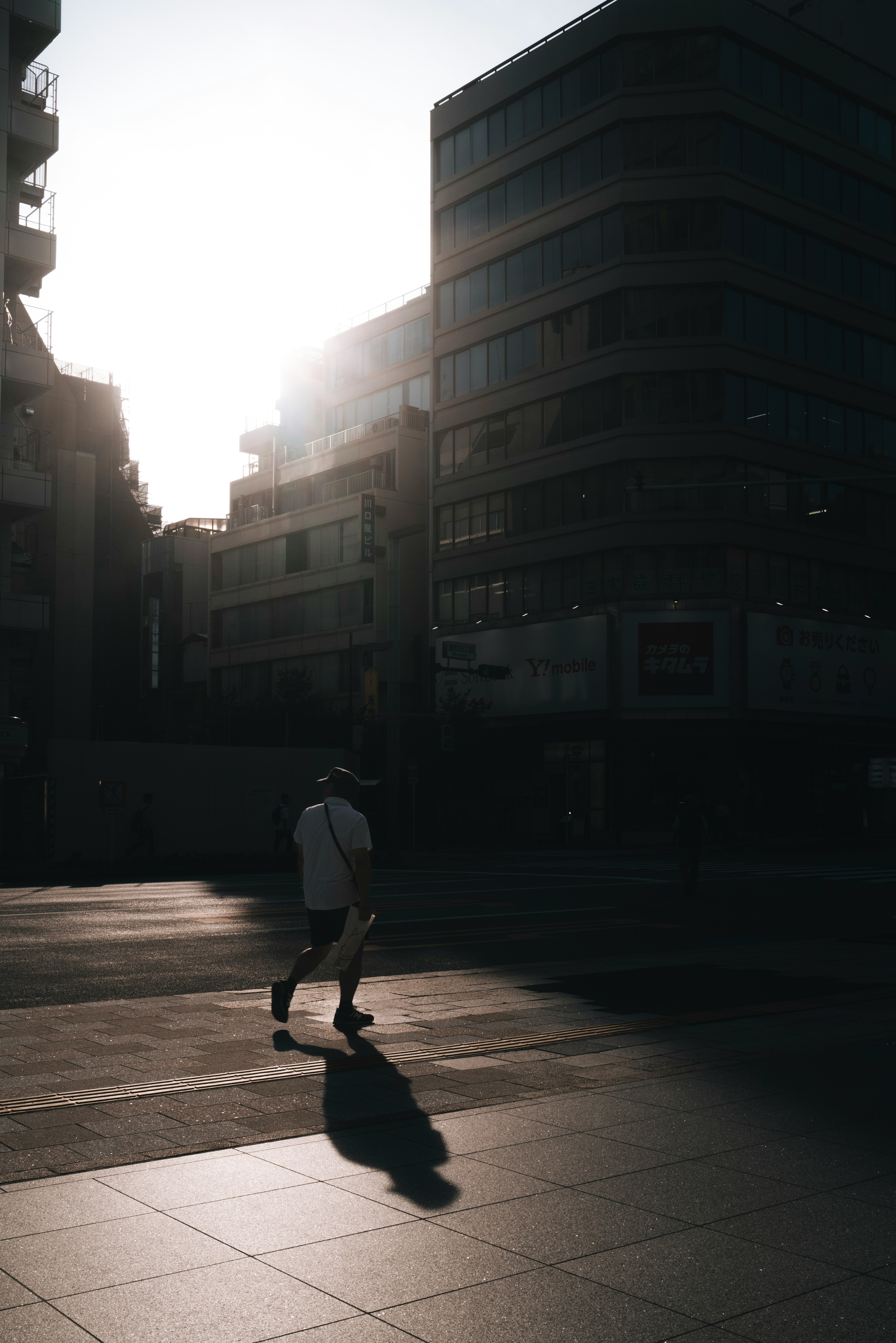 A silhouette of a person walking in a cityscape with bright sunlight