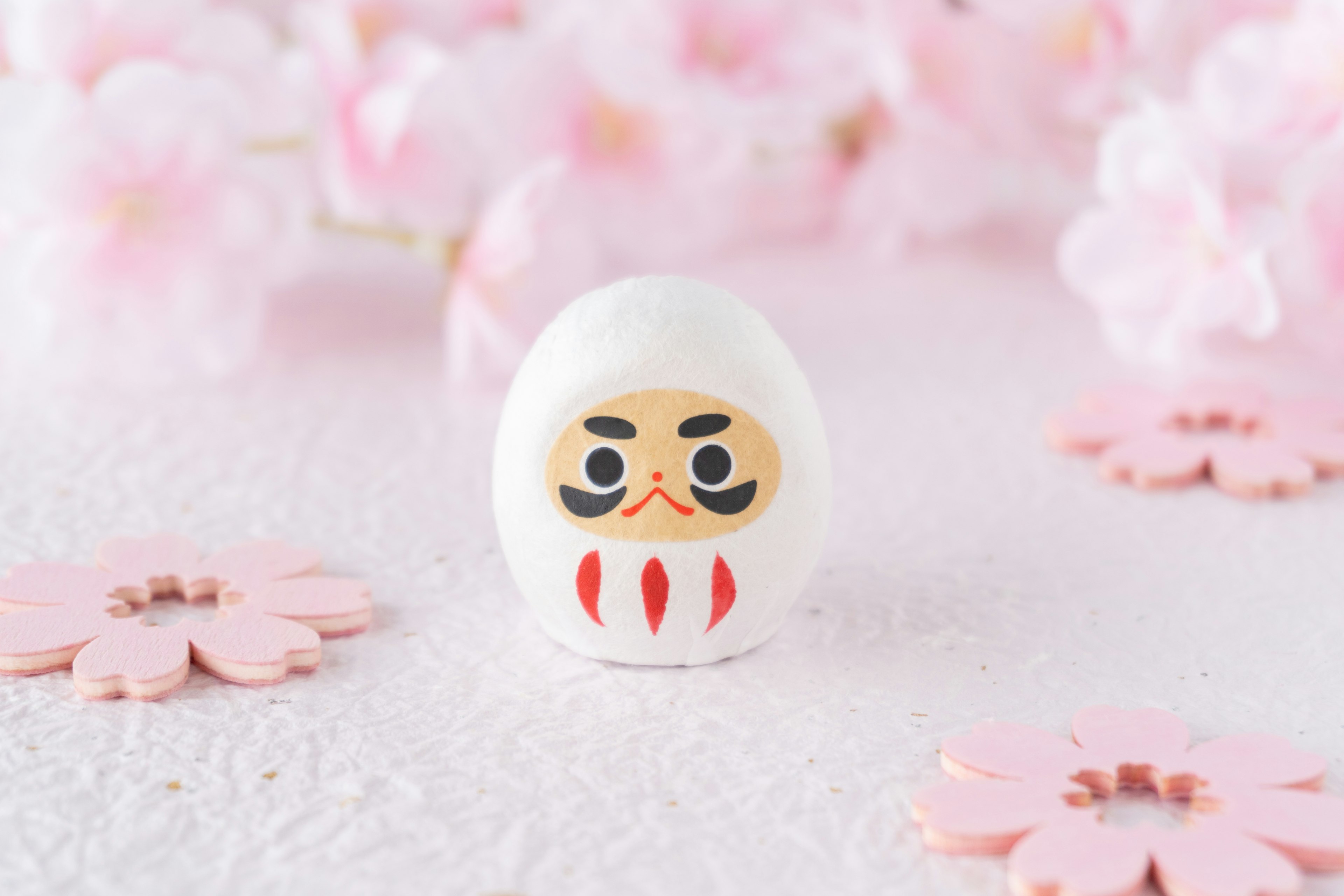 Poupée Daruma posée sur des pétales de cerisier roses