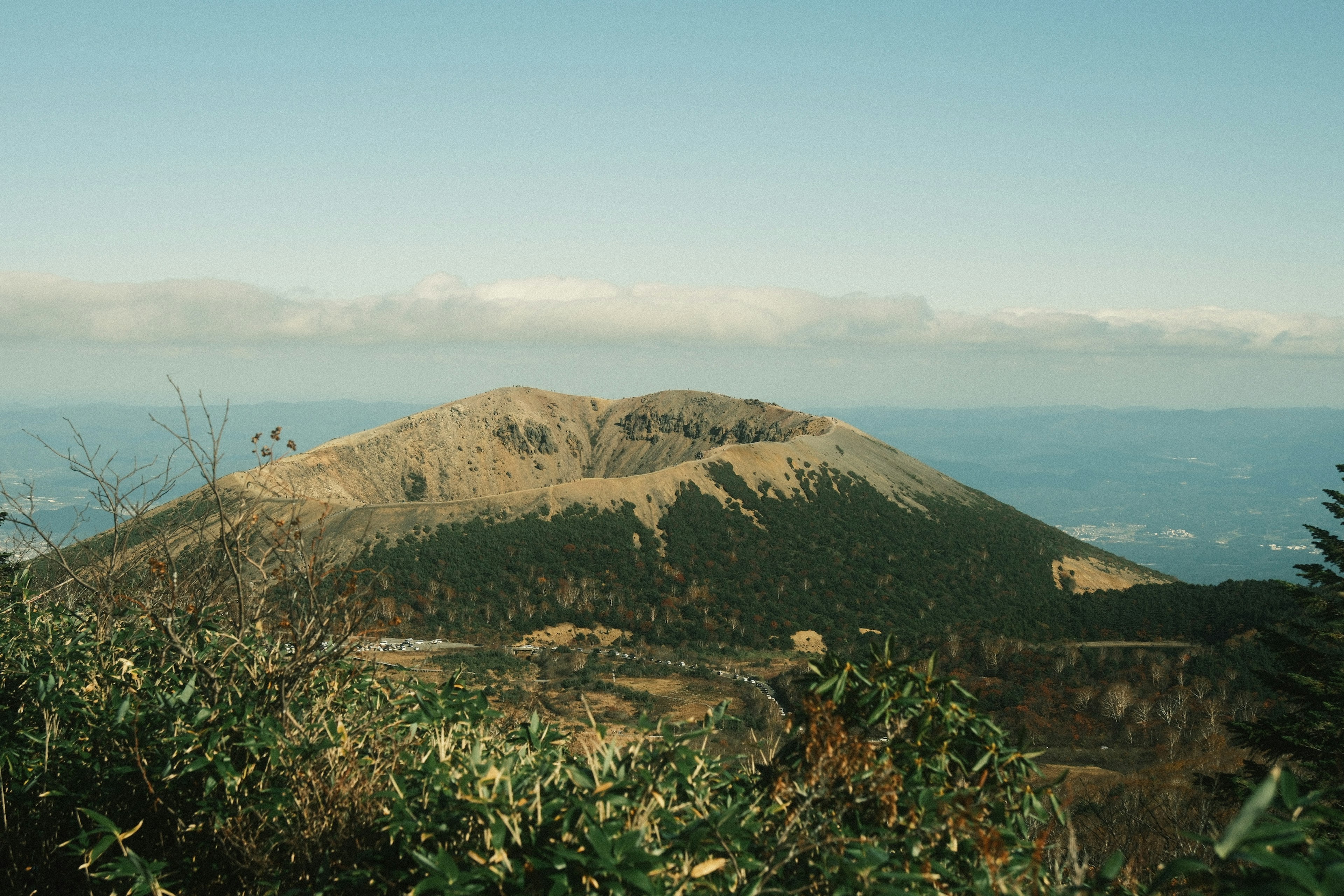 Pemandangan gunung vulkanik yang dikelilingi oleh tumbuhan hijau di bawah langit biru yang cerah