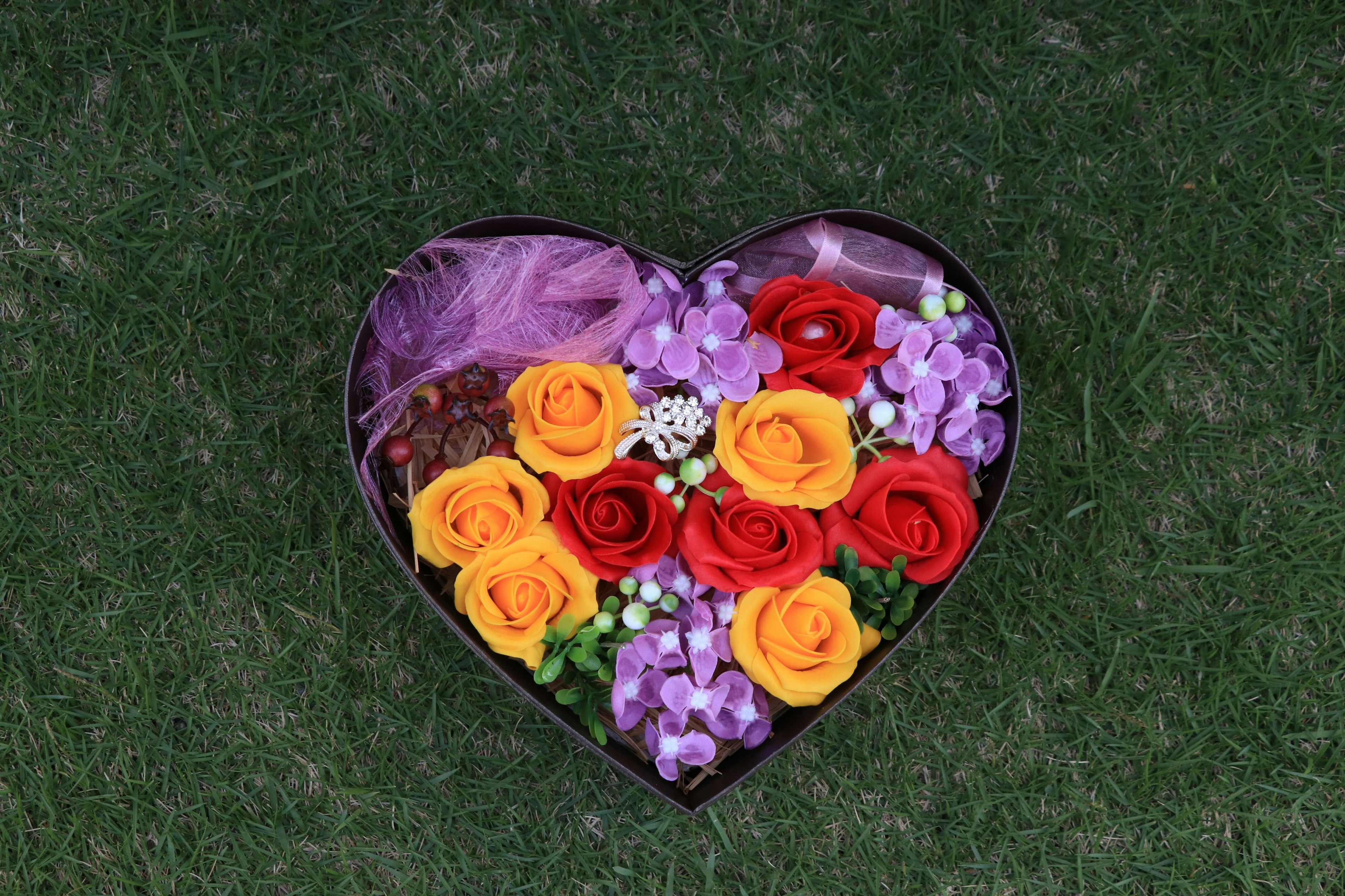 Arrangement floral en forme de cœur avec des roses colorées et des fleurs violettes