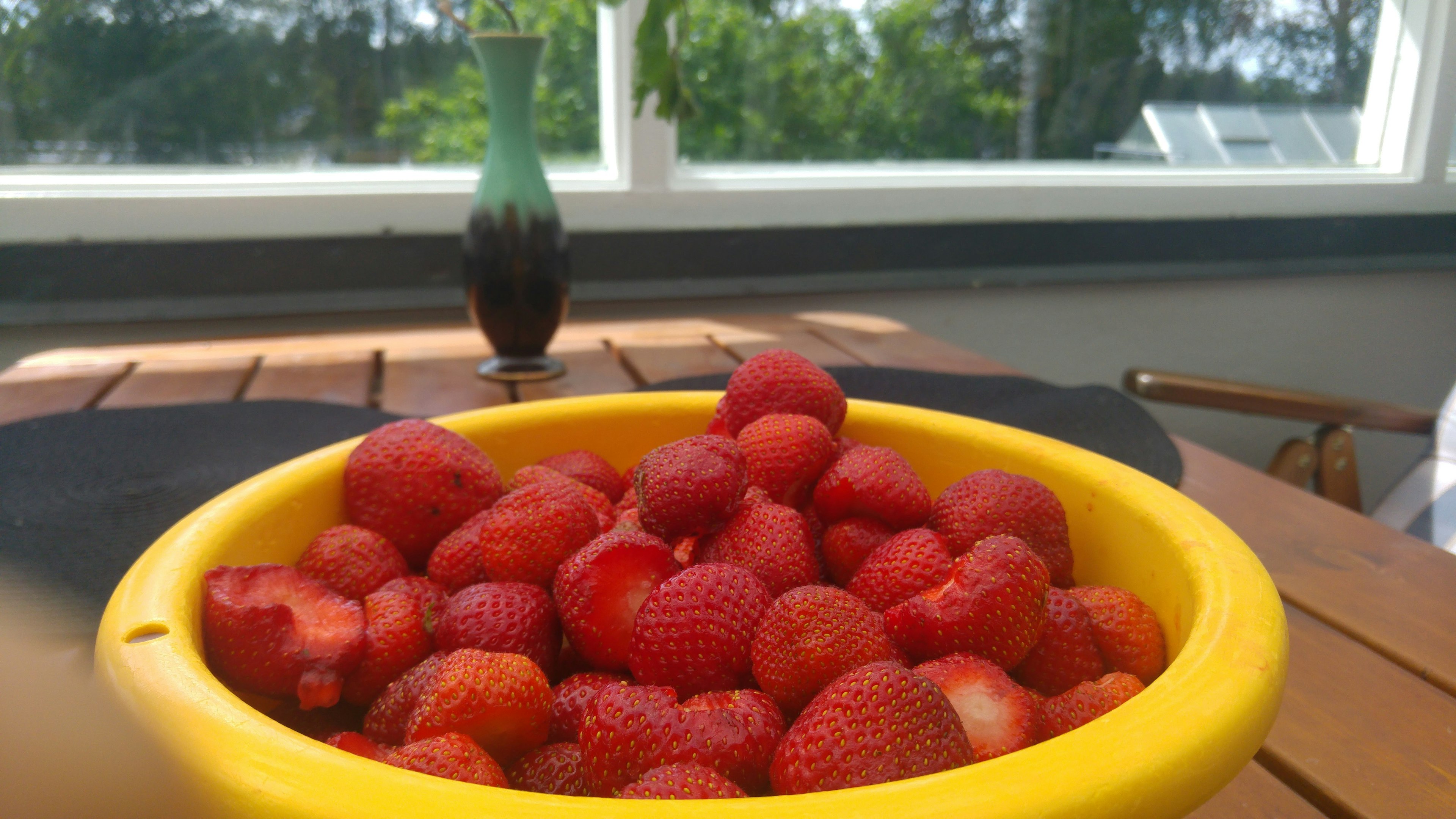 Fraises fraîches dans un bol jaune avec un fond vert et un vase décoratif