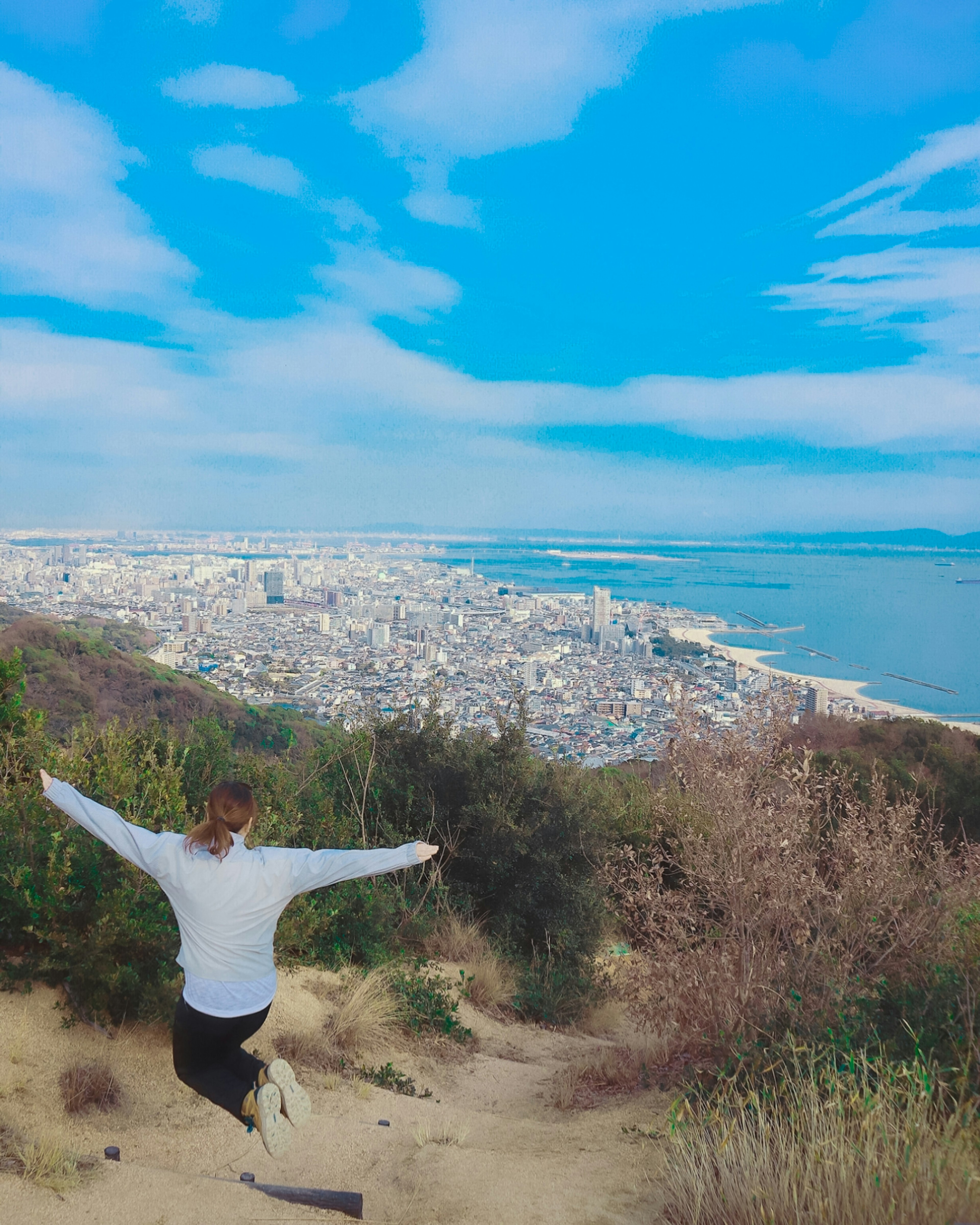 Mujer saltando con vista de la ciudad y el océano bajo un cielo azul