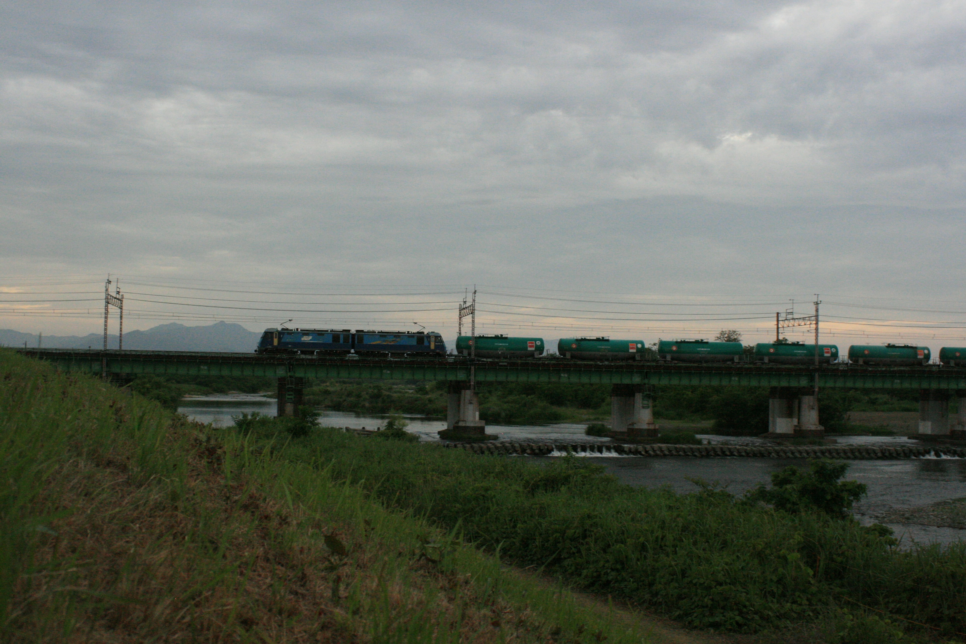 แถวของรถไฟสีน้ำเงินข้ามสะพานเหนือแม่น้ำท่ามกลางท้องฟ้าที่มีเมฆ